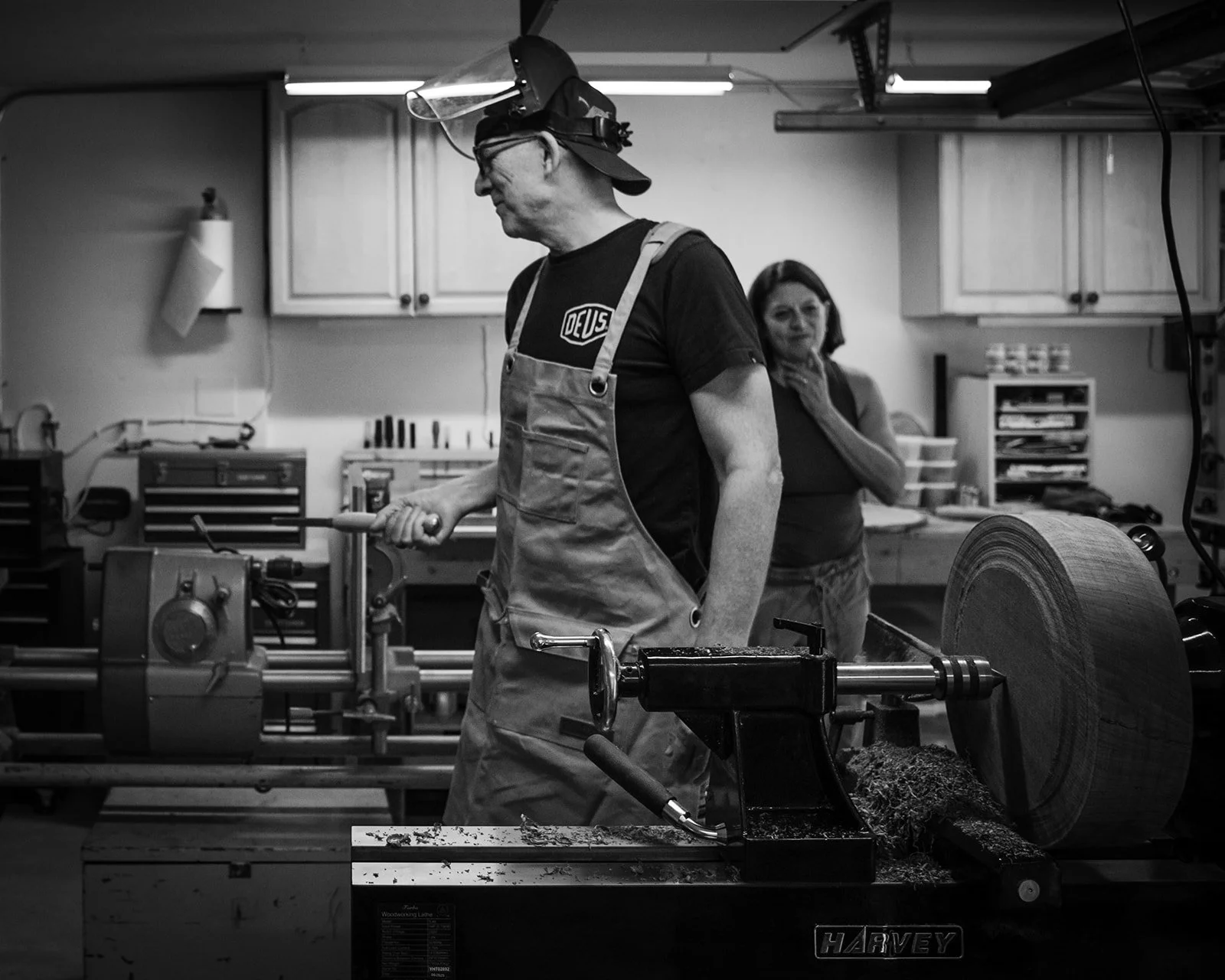 Rob Hodgson at the wood lathe with Paula looking on in the background, photographed by Christine Harris