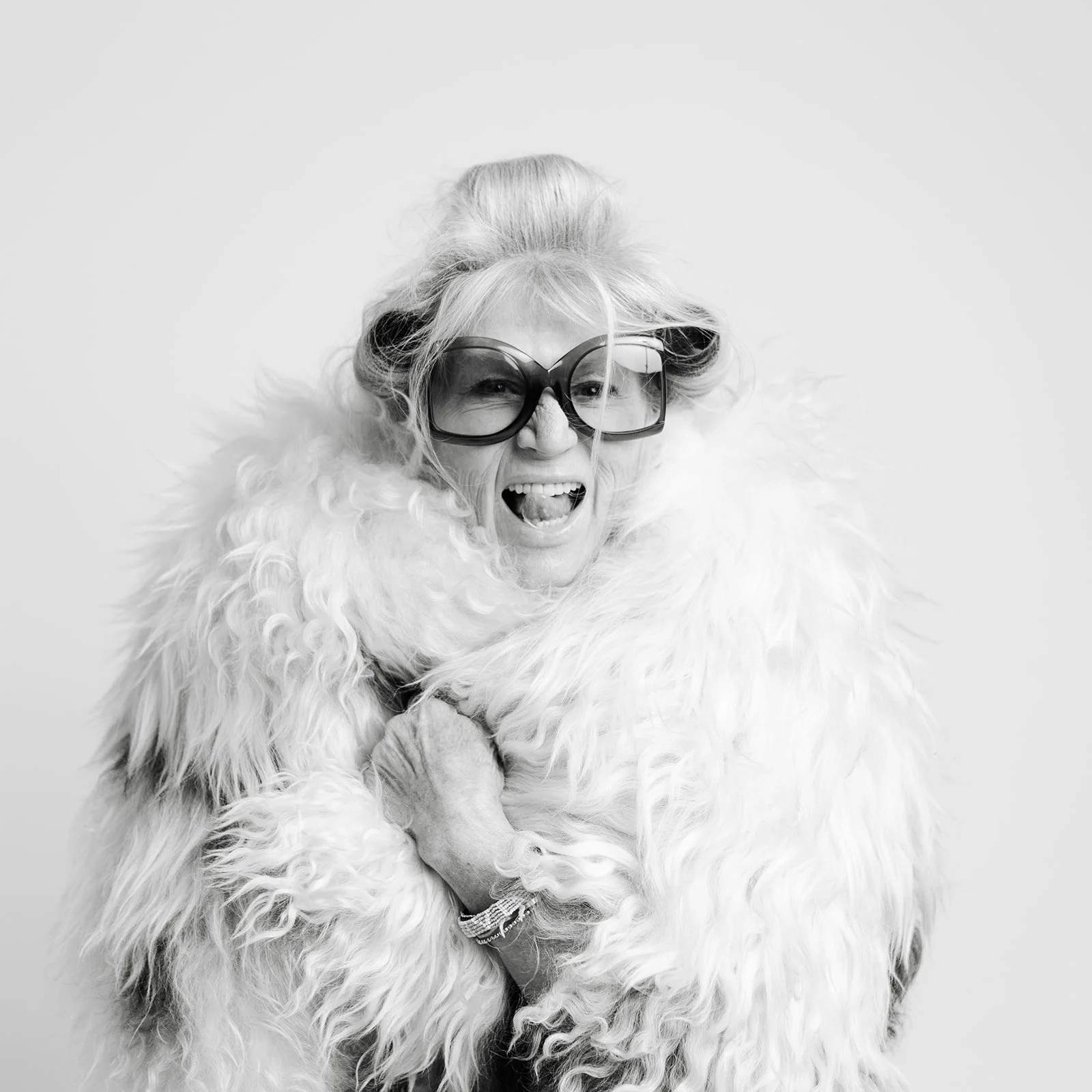Black-and-white portrait of Leigh Kilton-Smith laughing while wearing oversized glasses and a dramatic faux fur coat during her 50 Women Project session by Christine Harris.