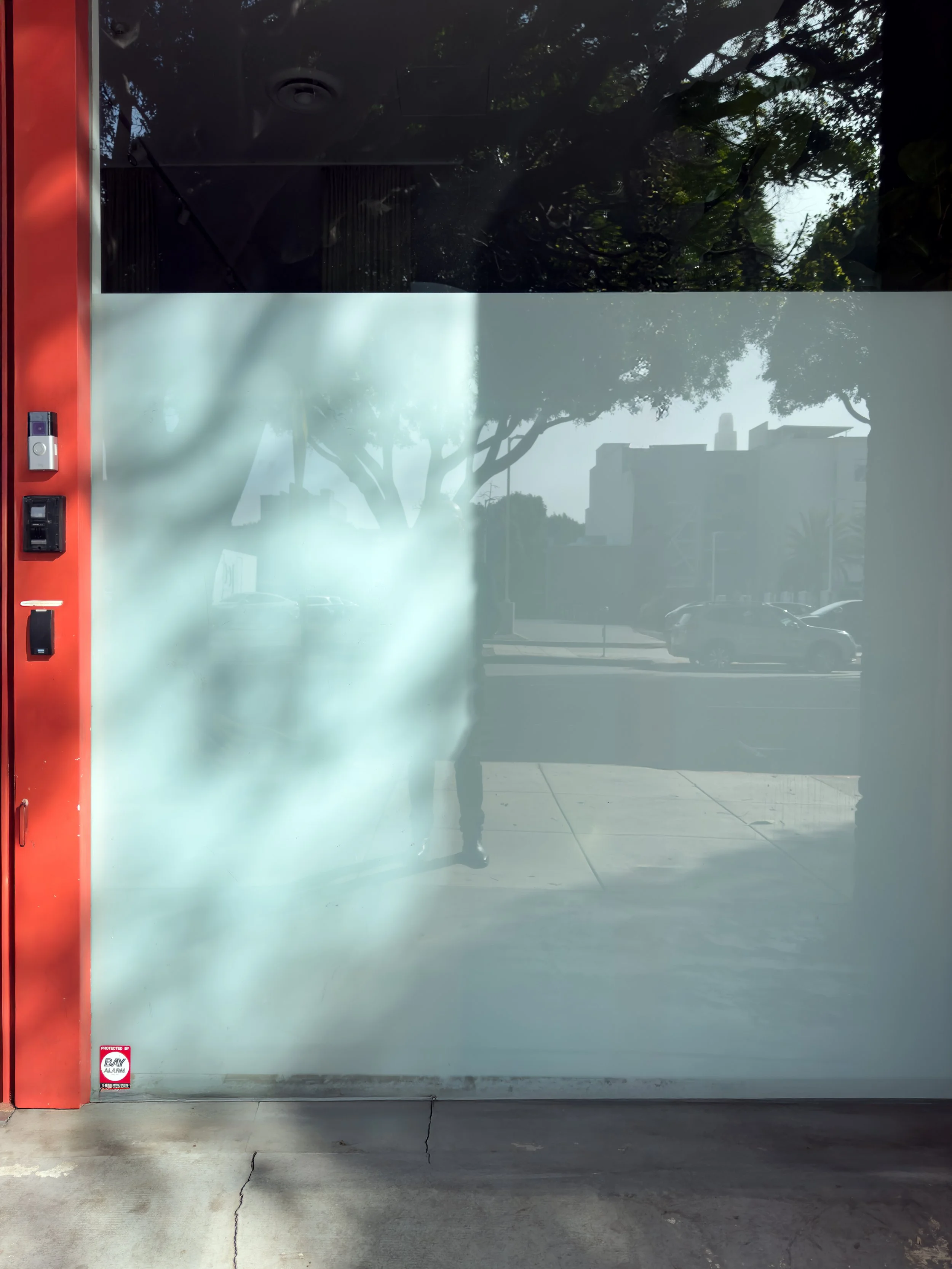 a glass storefront door with reflectors showing a sidewalk, trees, and buildings outside