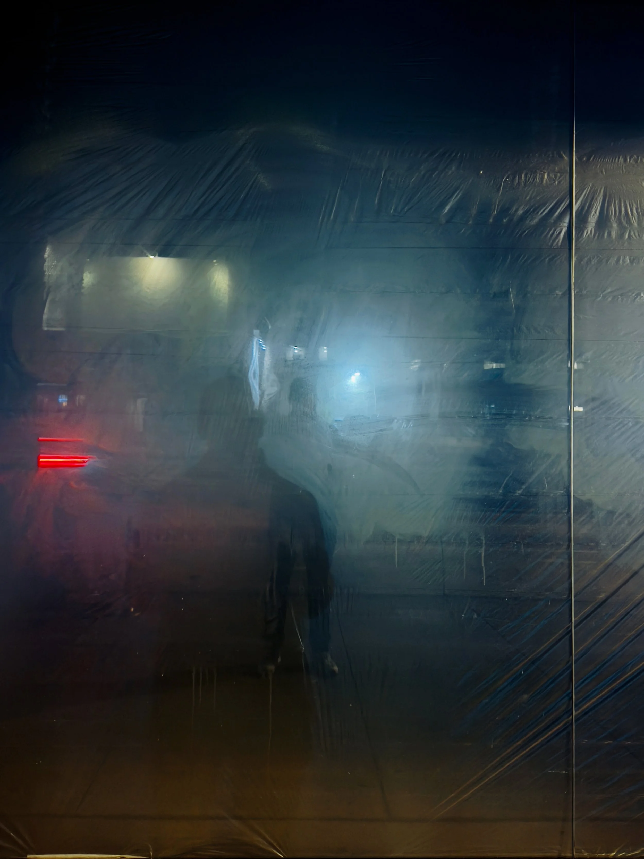 Blurry reflection of a person on a dark, transparent surface with dim lights and a red streak.