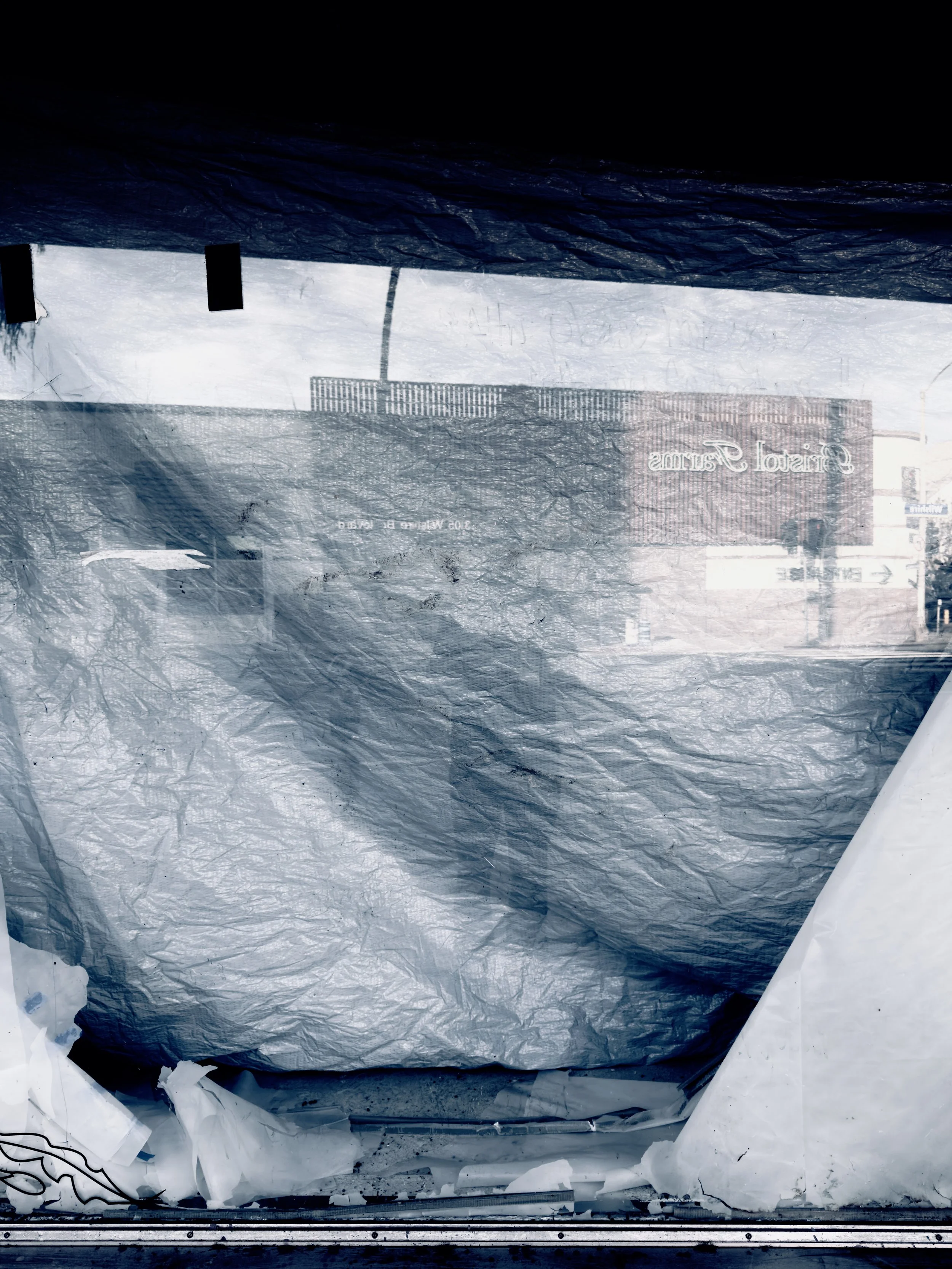 Snow-covered street view through a car window covered in ice and frost, with buildings and signs visible in the background.