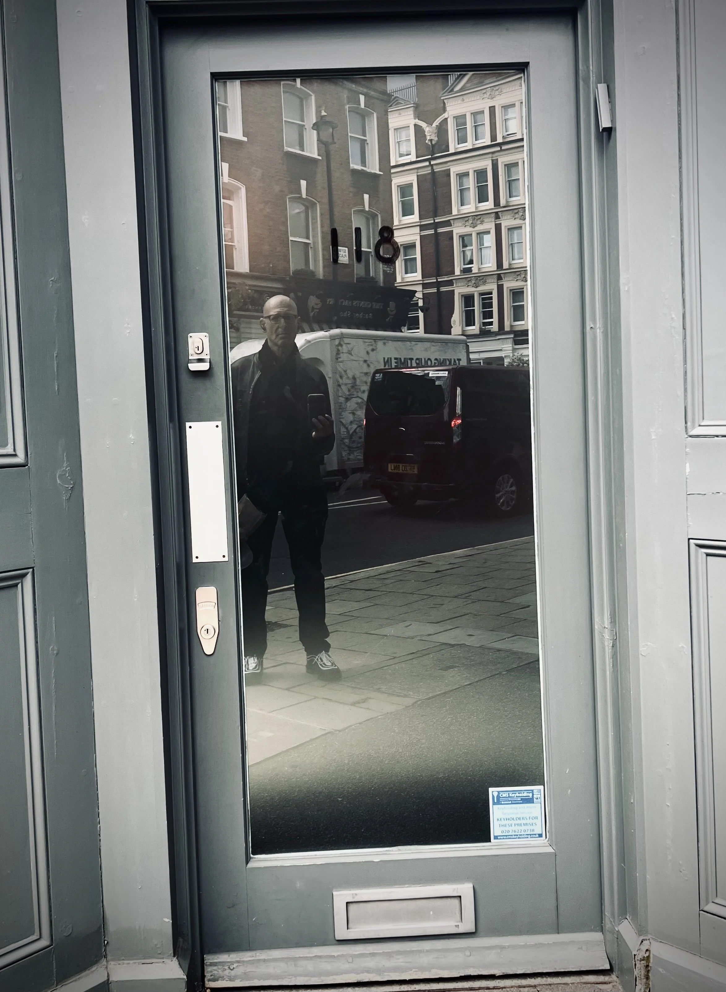 Reflection of a person taking a photo in glass door with buildings and vehicles in the background.