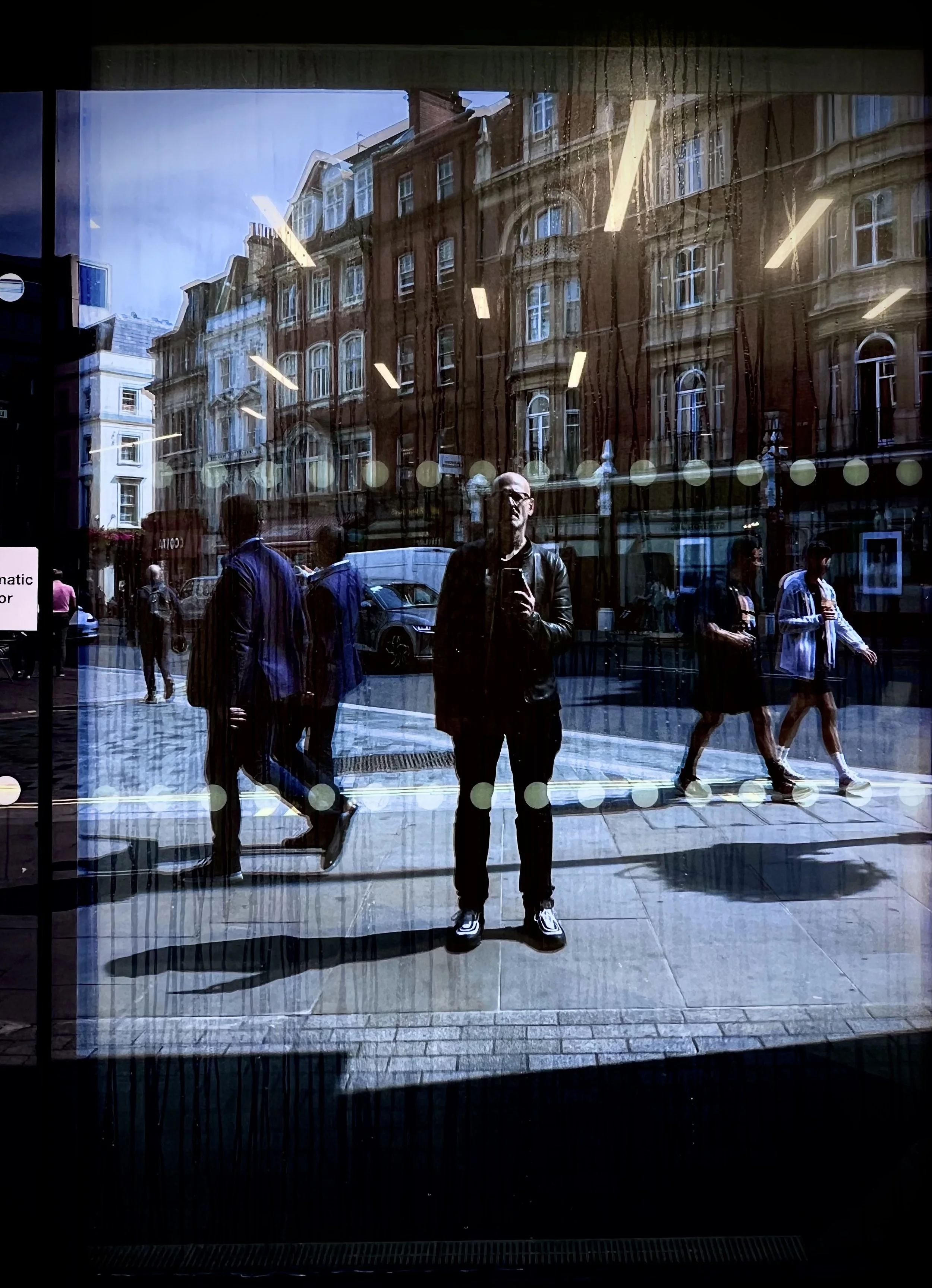 Reflection of people walking on city street and a person taking a selfie in storefront window during daytime.