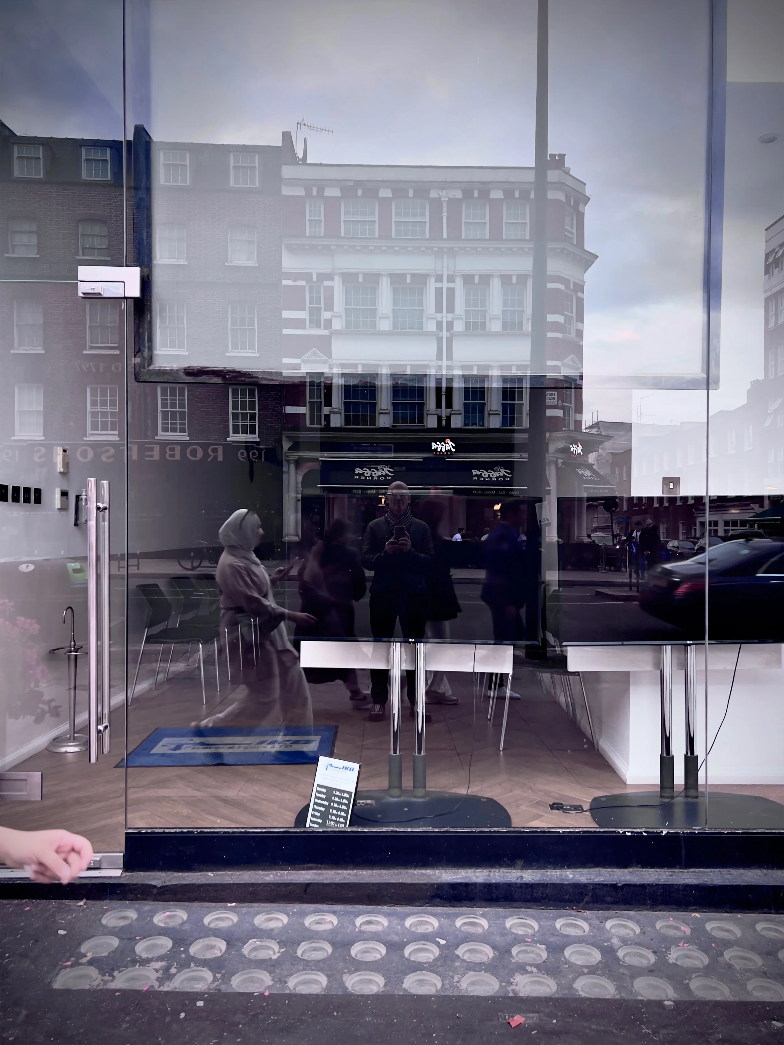 Reflective glass storefront door showing people inside and outside, with buildings and street scene reflected on the glass.