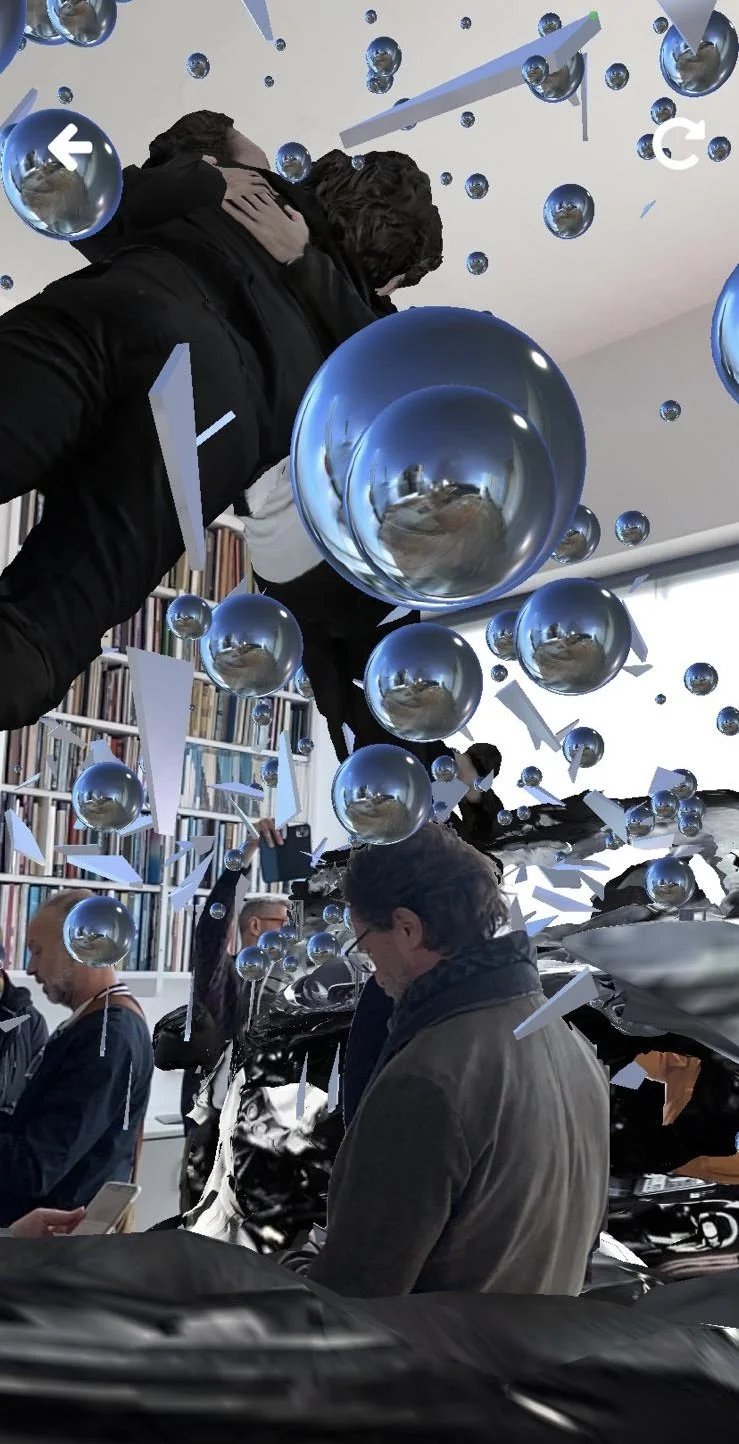 Digital art installation with people, reflective spheres, and fragmented objects in a room.