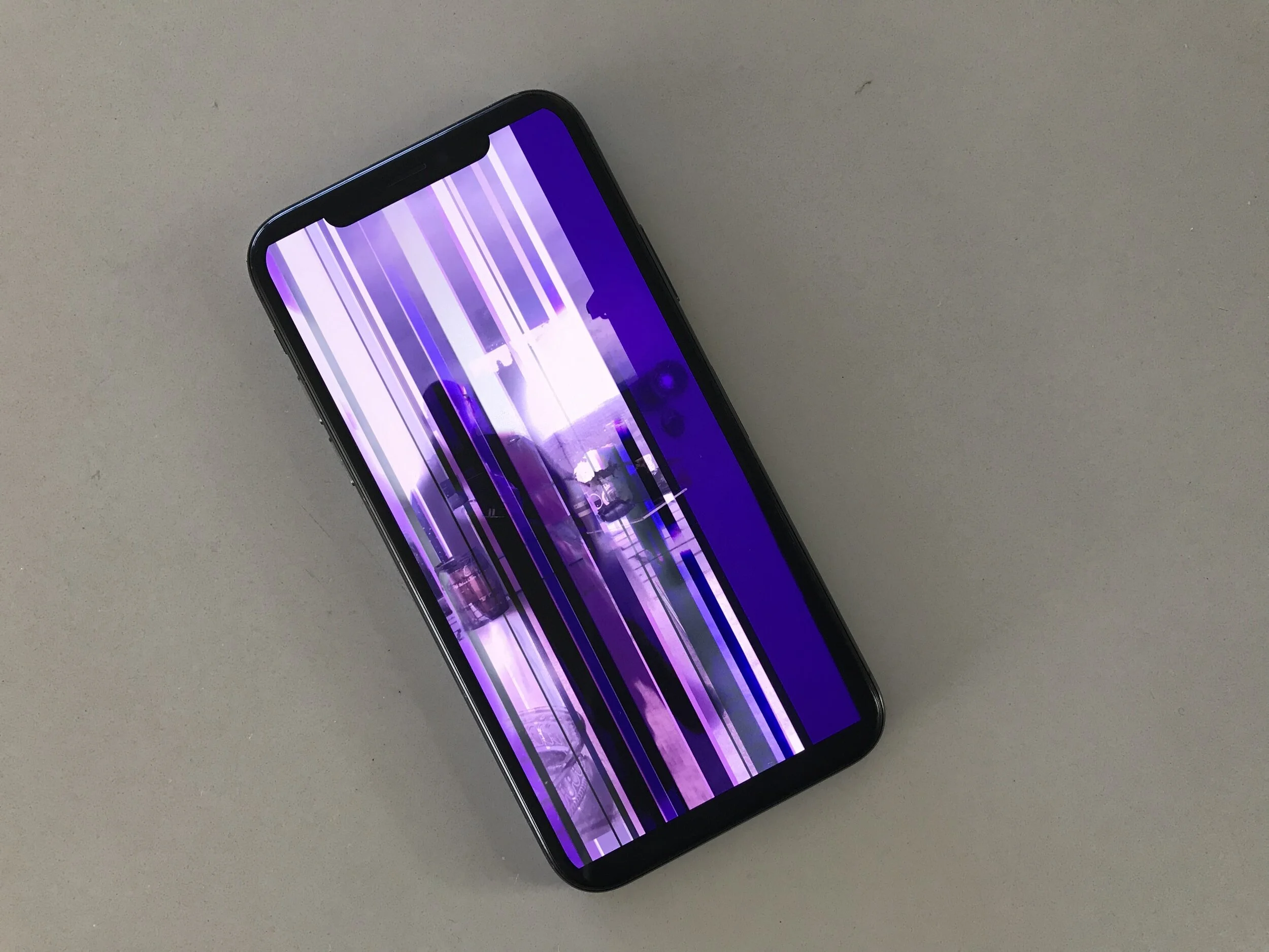 Smartphone with a damaged screen displaying distorted purple vertical lines on a gray background.
