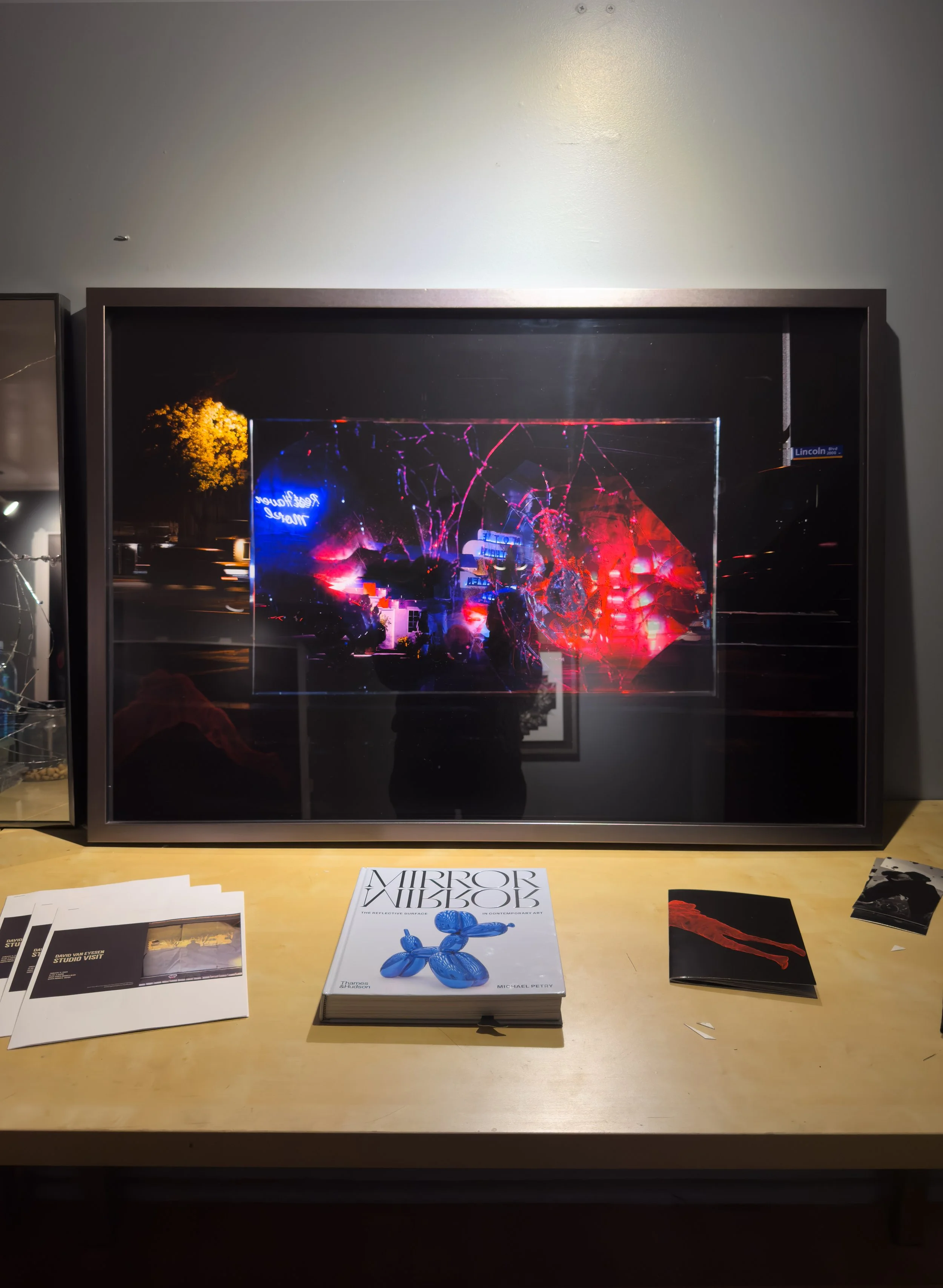 Framed abstract artwork on a wall above a table with books and pamphlets