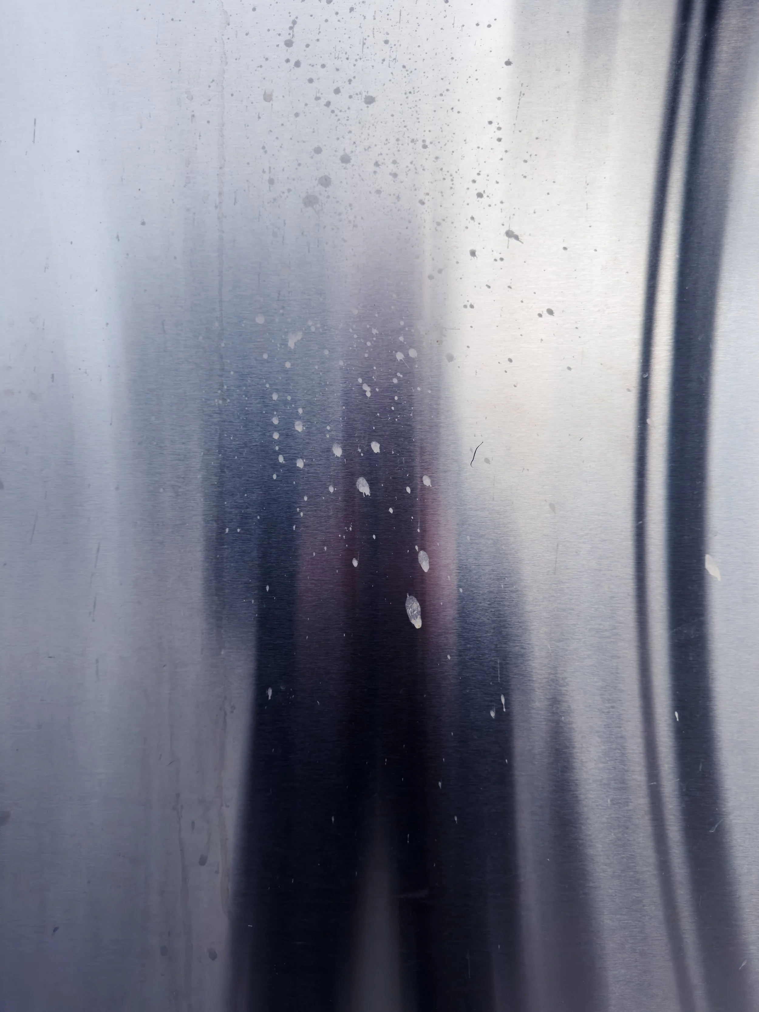 Frosted glass door with water spots and a blurry reflection of a person taking a photo.