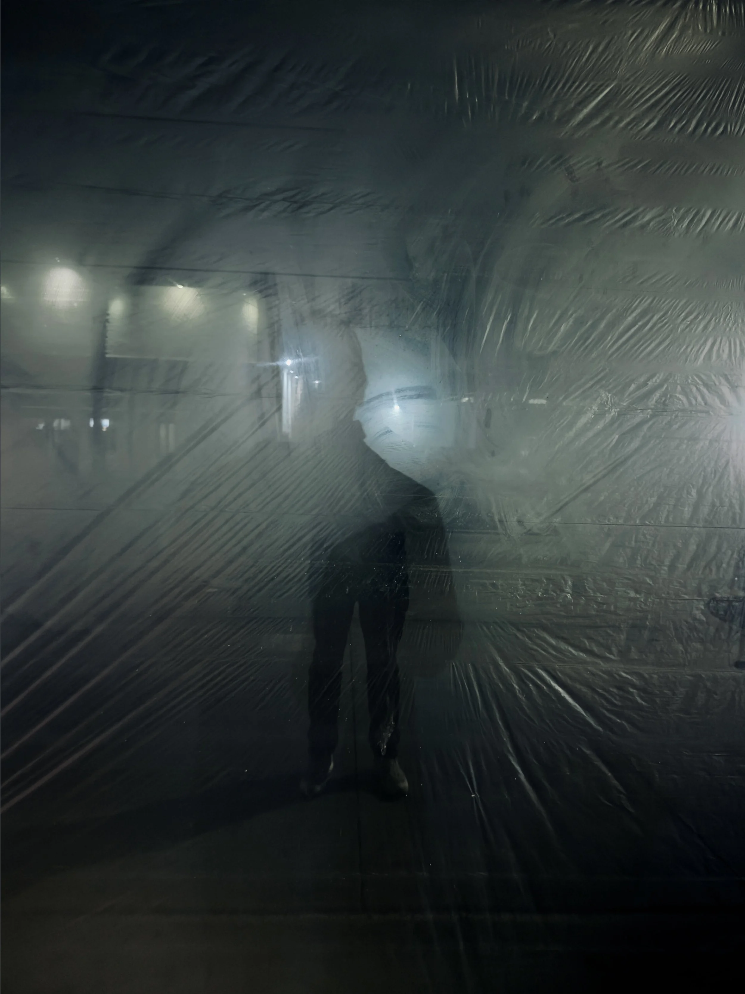 Silhouette of a person behind a sheet of plastic with dim lights in the background.