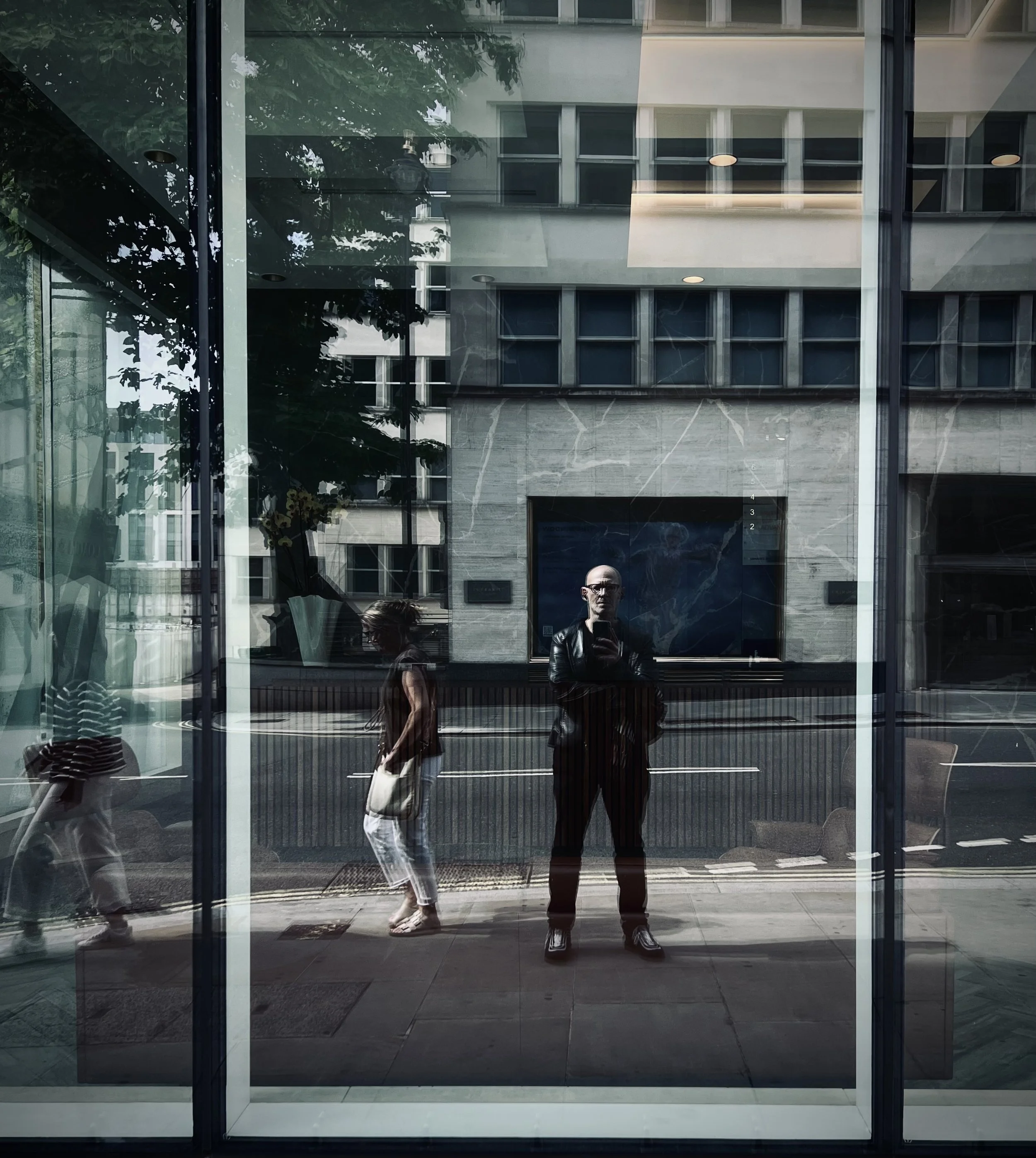 Reflection of people walking by glass windows on a city street with a building in the background.
