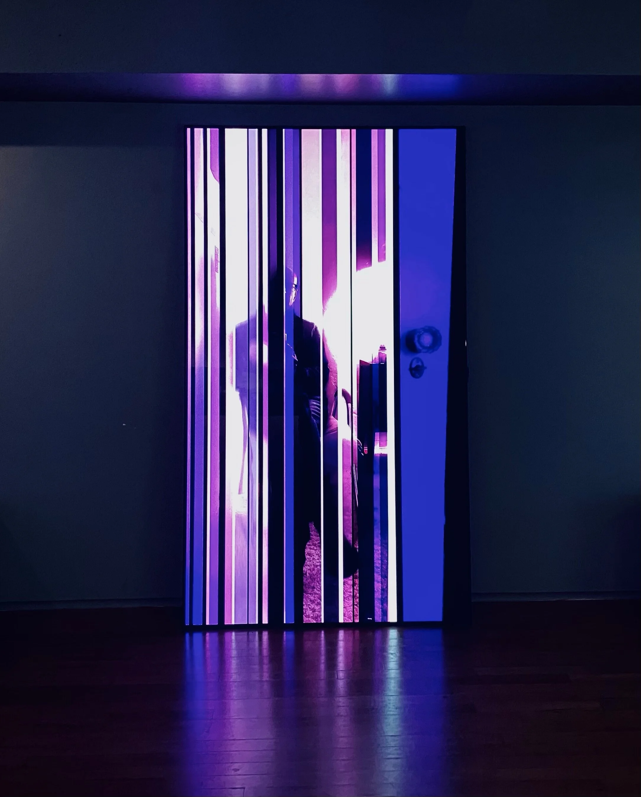 Illuminated doorway with a silhouetted figure behind vertical light strips.