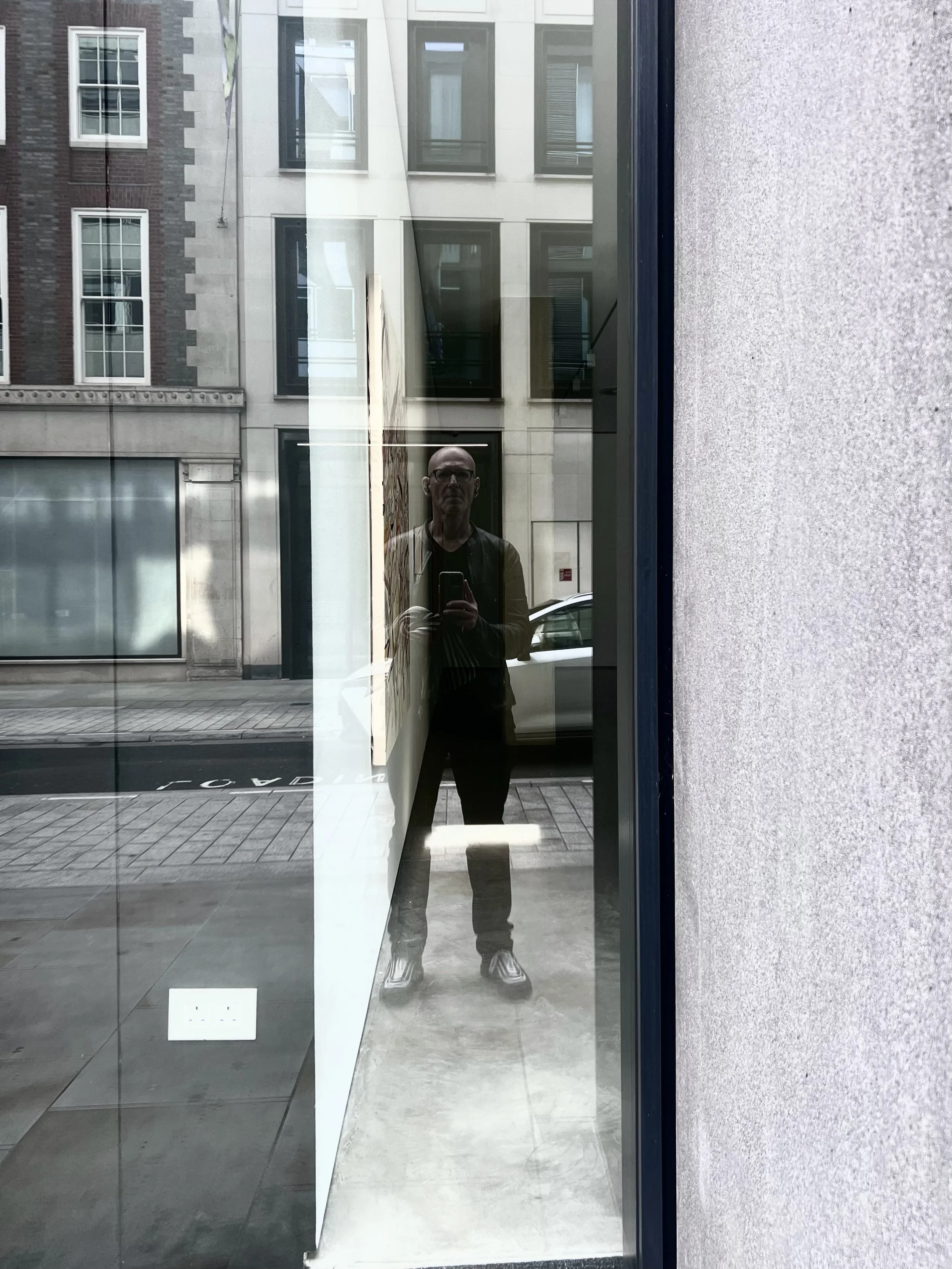 Reflection of a person in a window on a city street with buildings in the background.