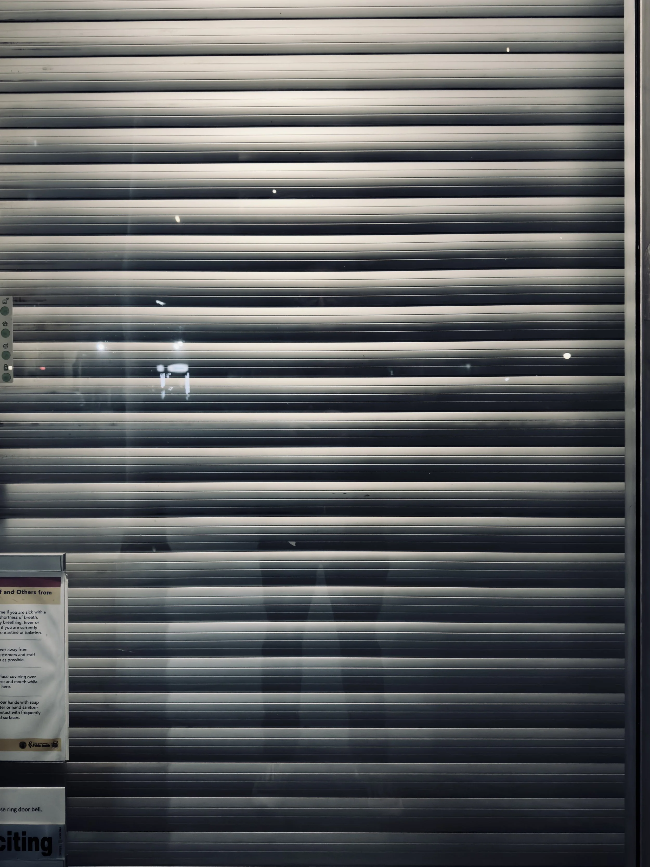 Closed metal roll-up door with a reflection of people and signs in front of it.