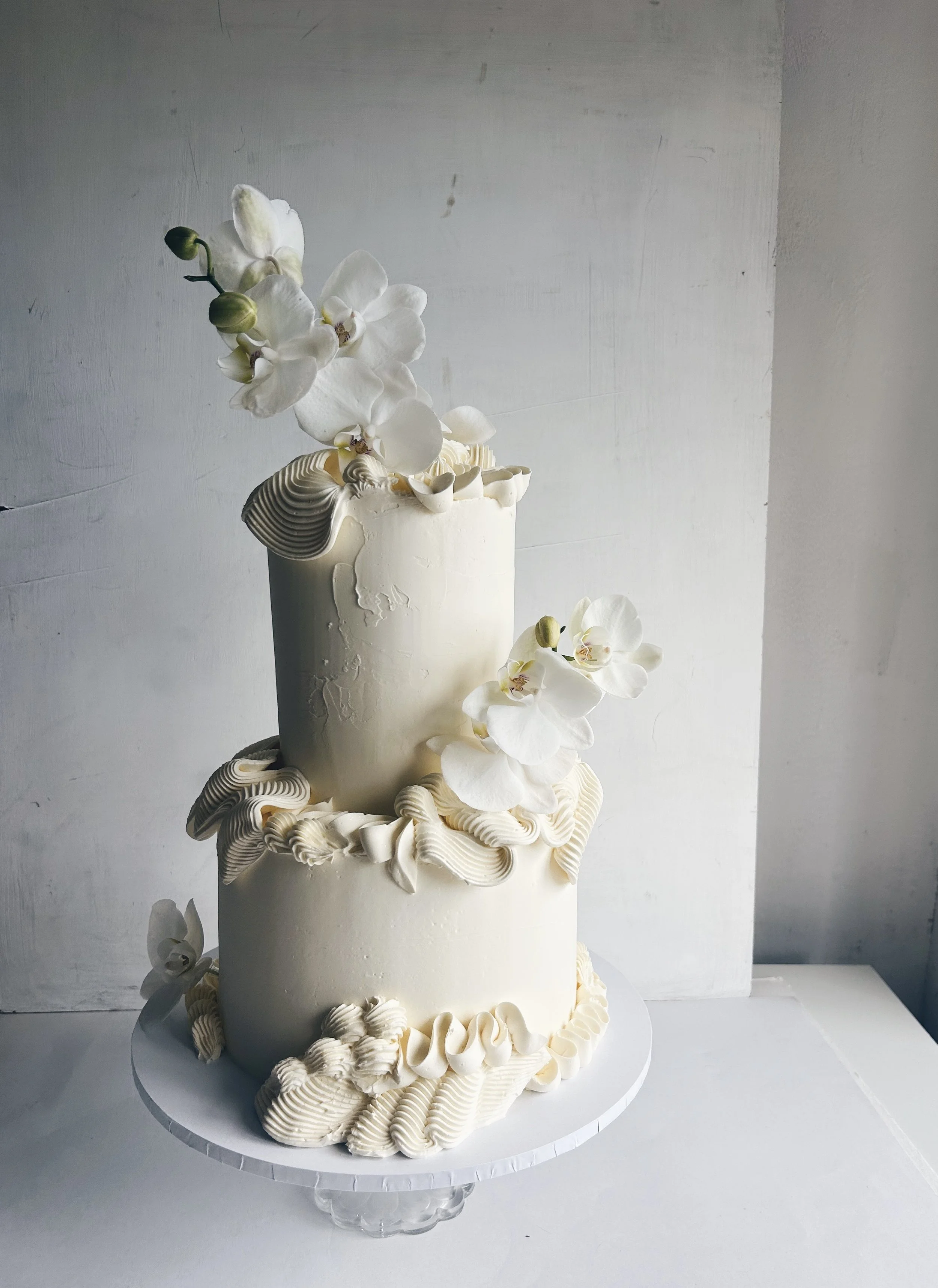 A two-tiered white wedding cake decorated with white orchids and cream-colored piping.