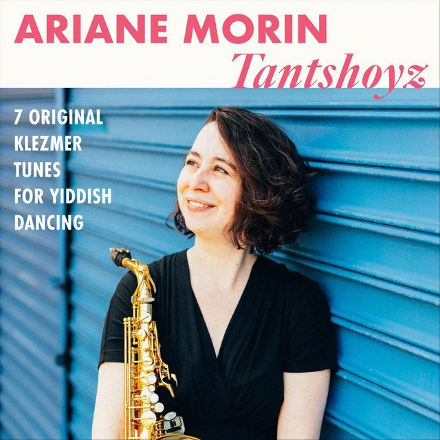 Woman with short curly hair holding a saxophone, standing against a blue corrugated wall, smiling, on an album cover titled "Tantshvoyz" by Ariane Morin  featuring 7 original Klezmer tunes for Yiddish dancing.