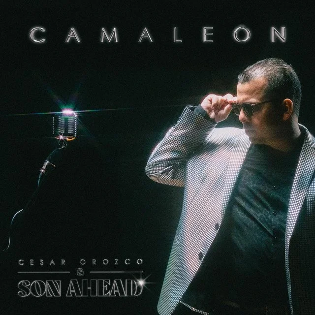 Cover art for Cesar Orozco's album "Son Ahead" featuring Cesar Orozco wearing sunglasses and a checkered blazer, adjusting his glasses in front of a black background with the text "Cameleón" at the top and "Cesar Orozco - Son Ahead" at the bottom.