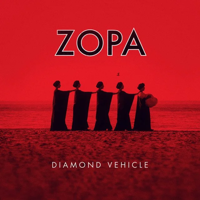 Red-tinted image of five women in long dresses and hats walking on the beach, with a bird flying overhead. The text reads "ZOPA" at the top and "Diamond Vehicle" at the bottom. Album artwork for "Diamond Vehicle" by Zopa.