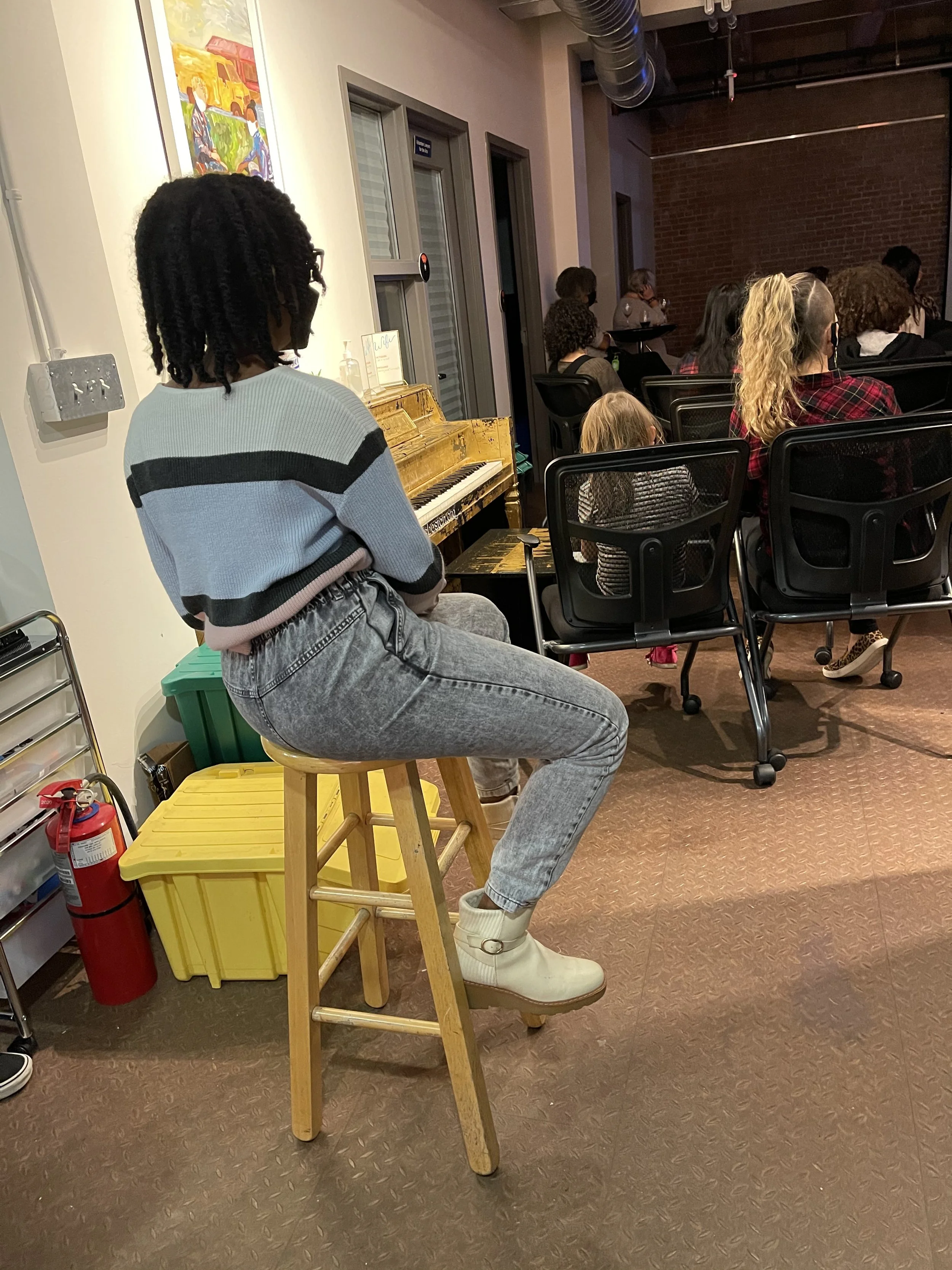 Lia sits on a stool listening to the panel discussion. 