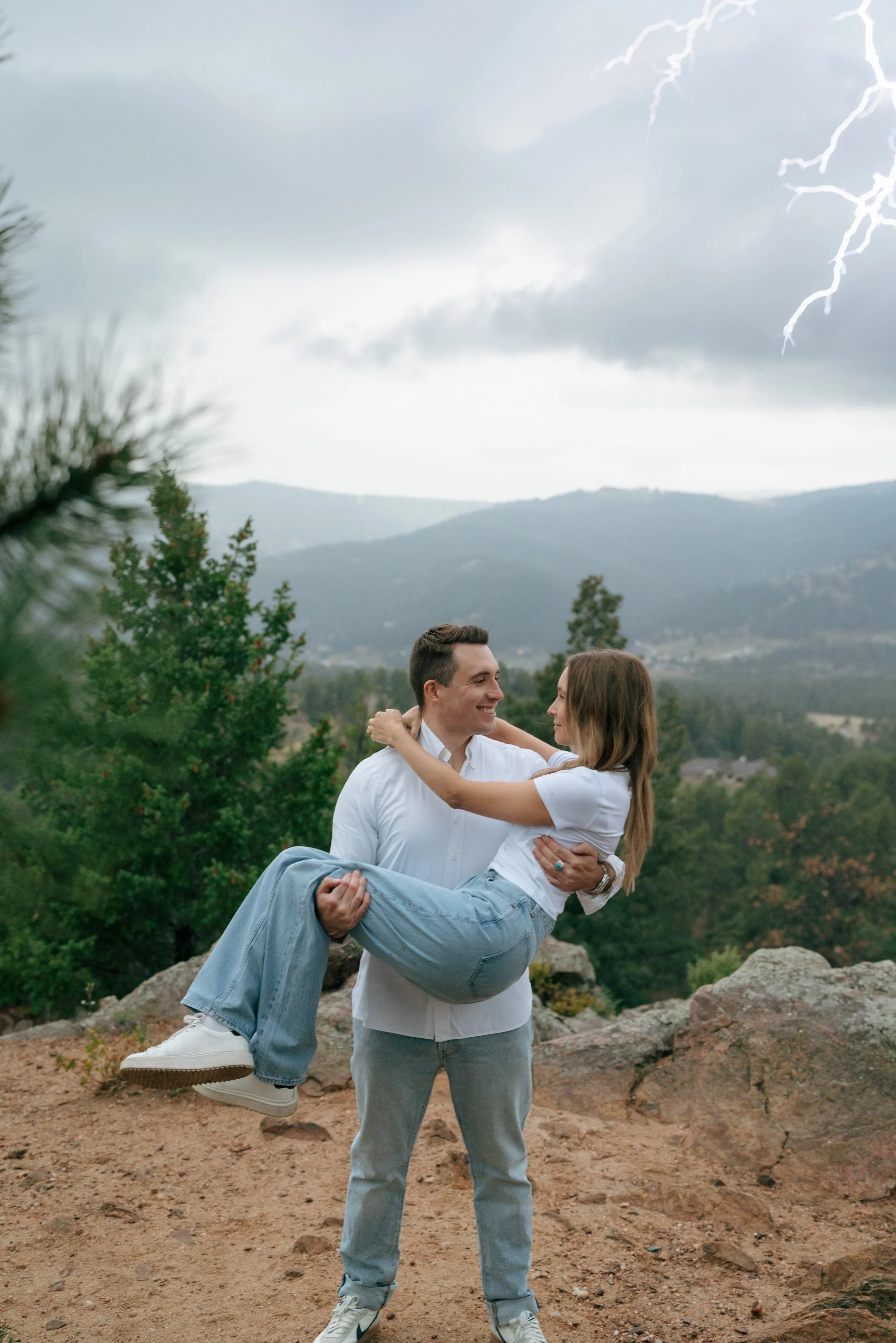 a man holding a woman as lightning strikes above them during their engagement photoshoot