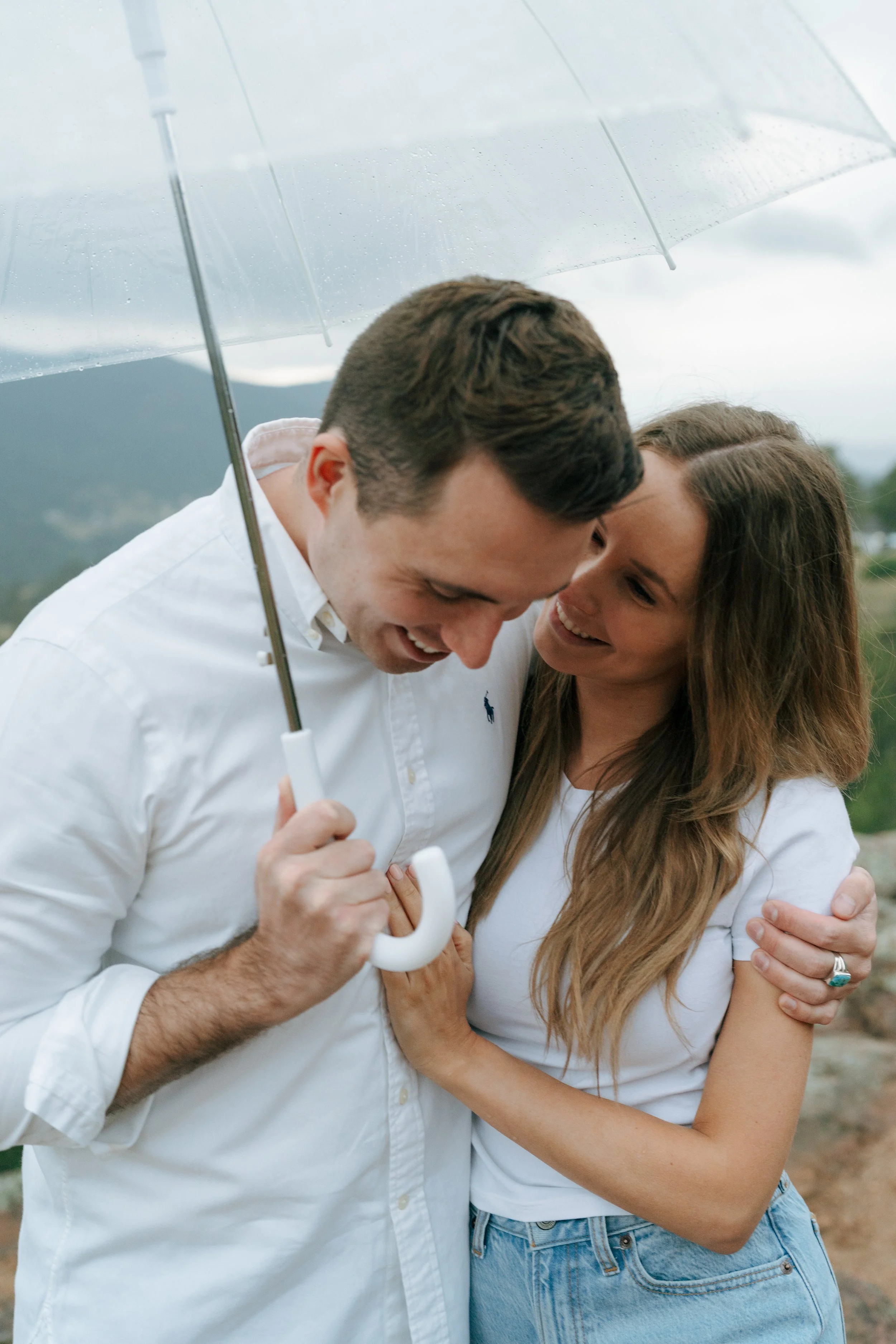 a couple smiling together under an umbrella during their cinematic engagement photoshoot