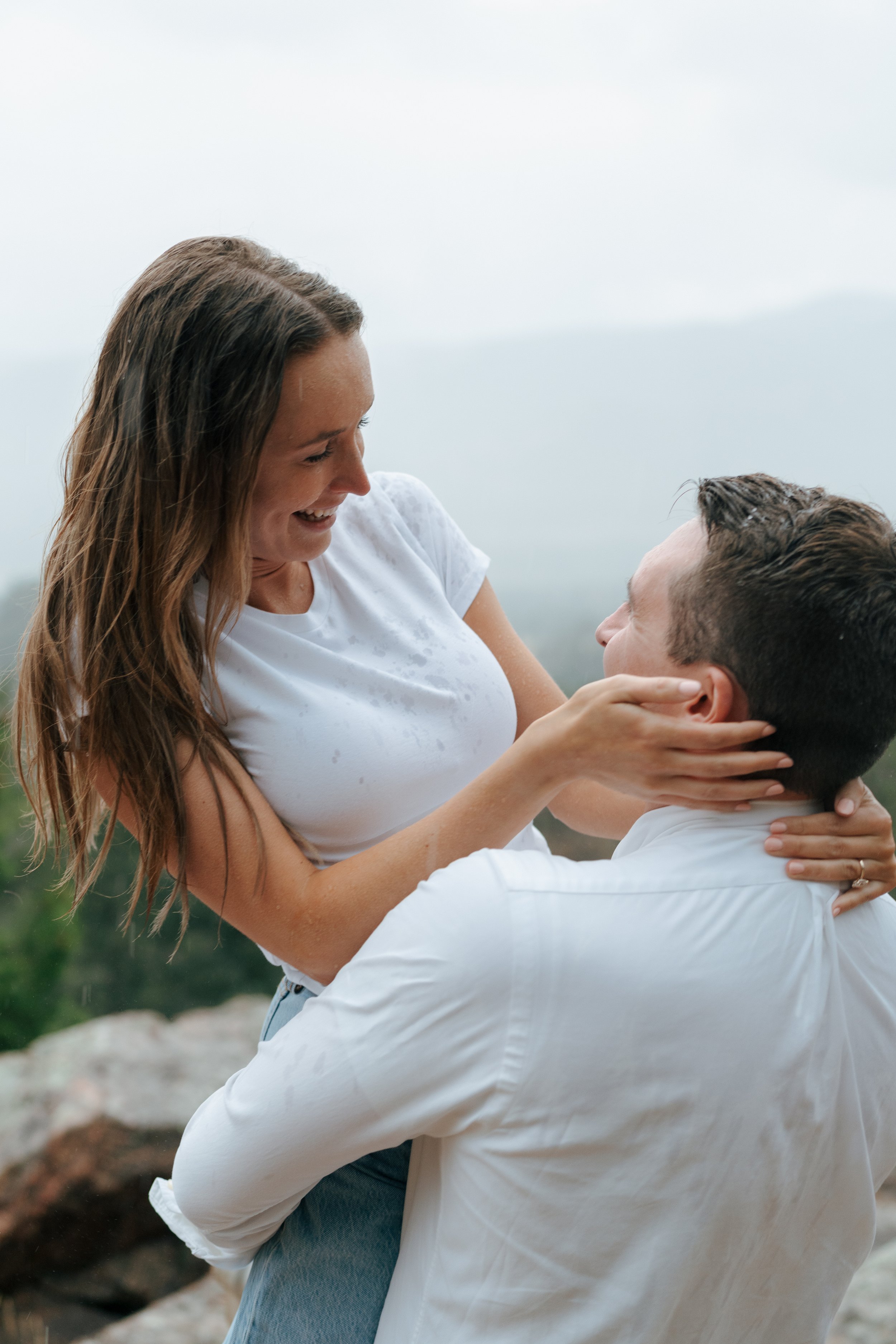 a man holding up a woman as they smile at each other during an engagement photoshoot