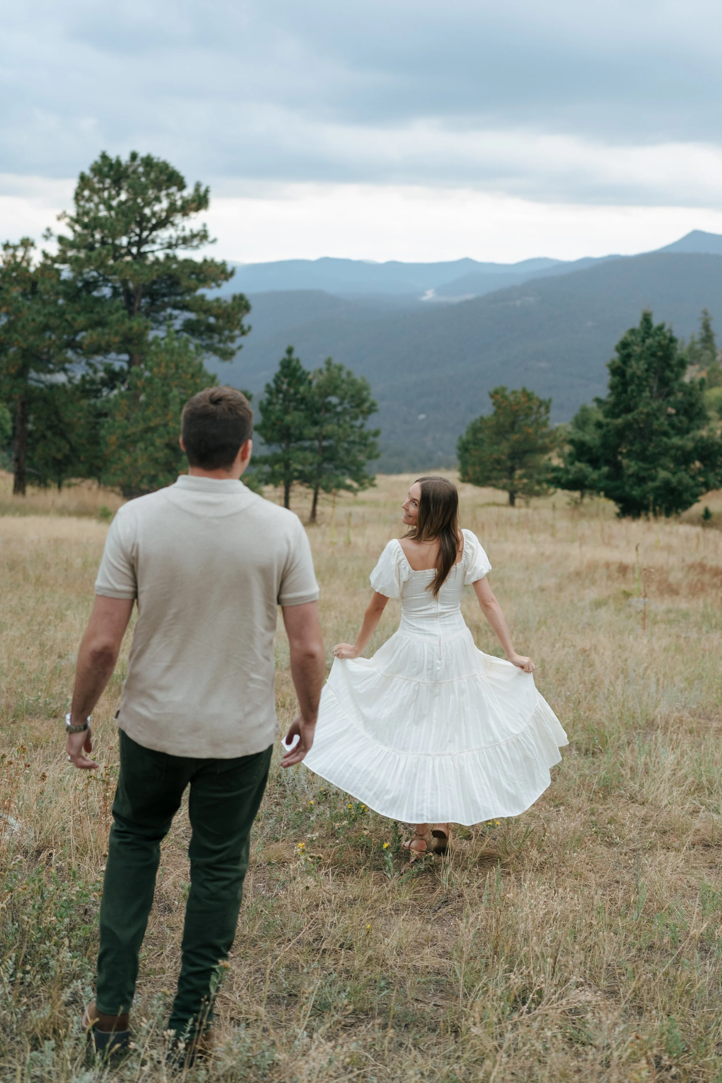 a woman holding out her dress at the sides as she looks back at a man during their engagement photoshoot
