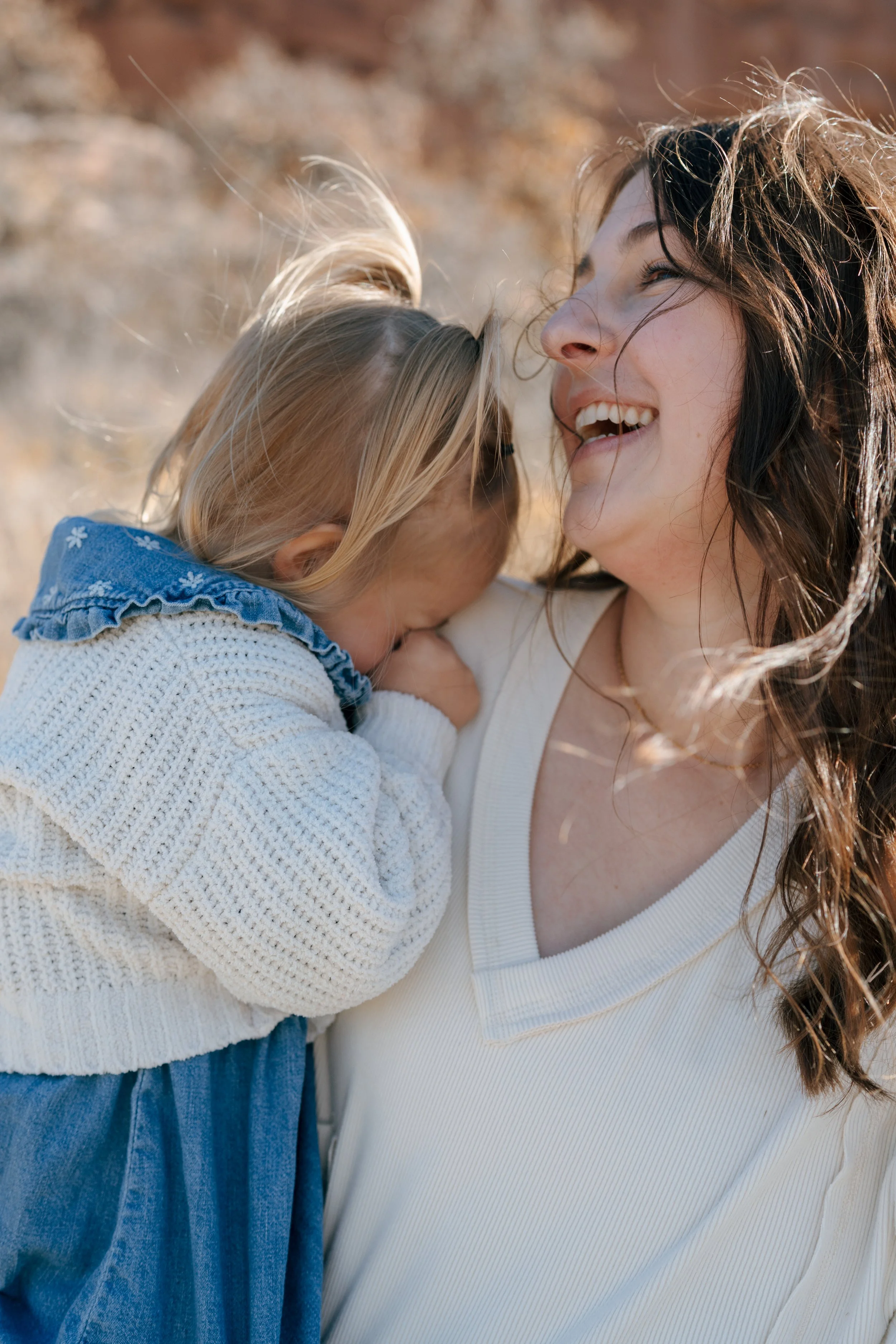 a mom laughing as she holds her daughter close during a family photo session