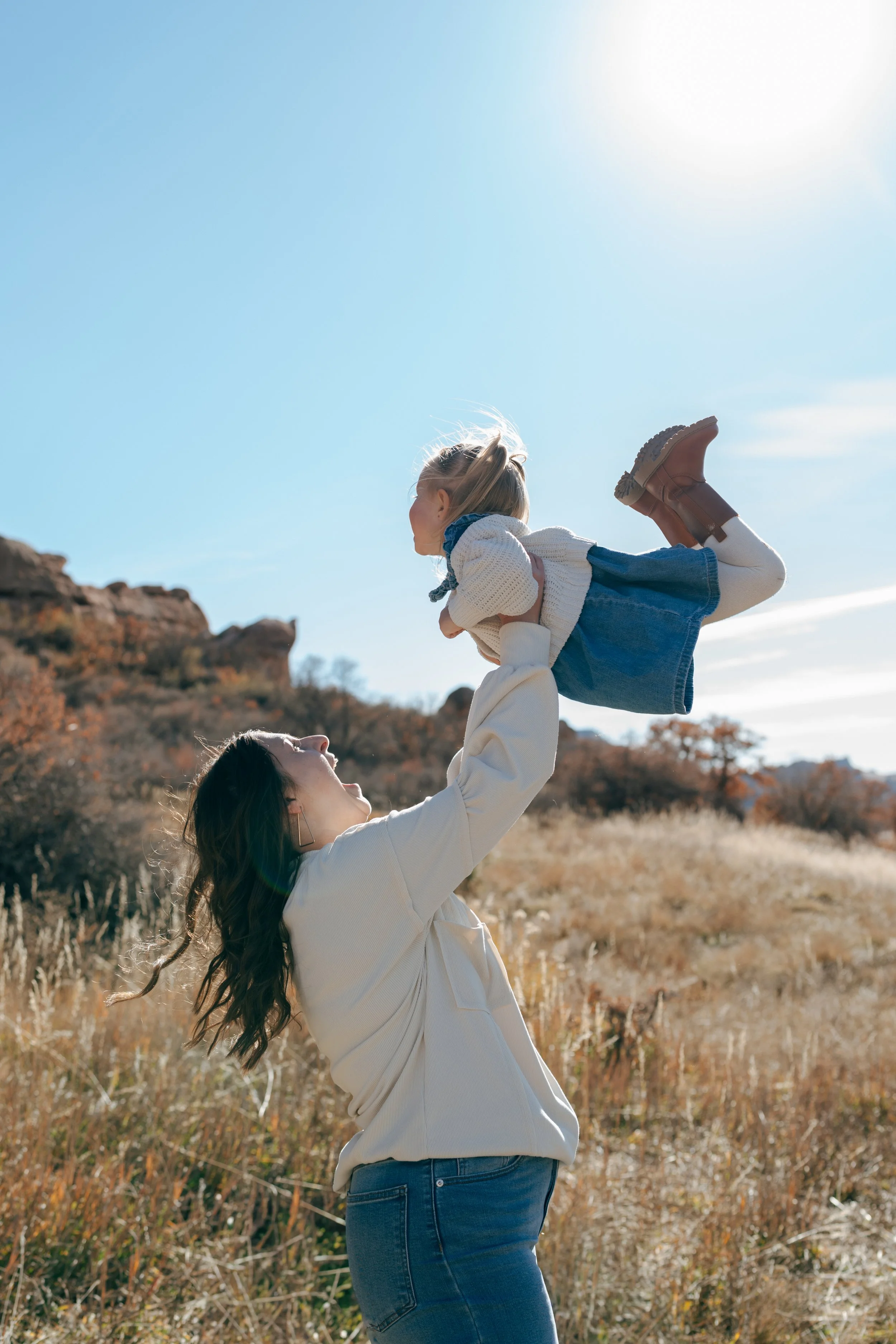 a mom throwing her daughter up in the air during a family photo session in Colorado
