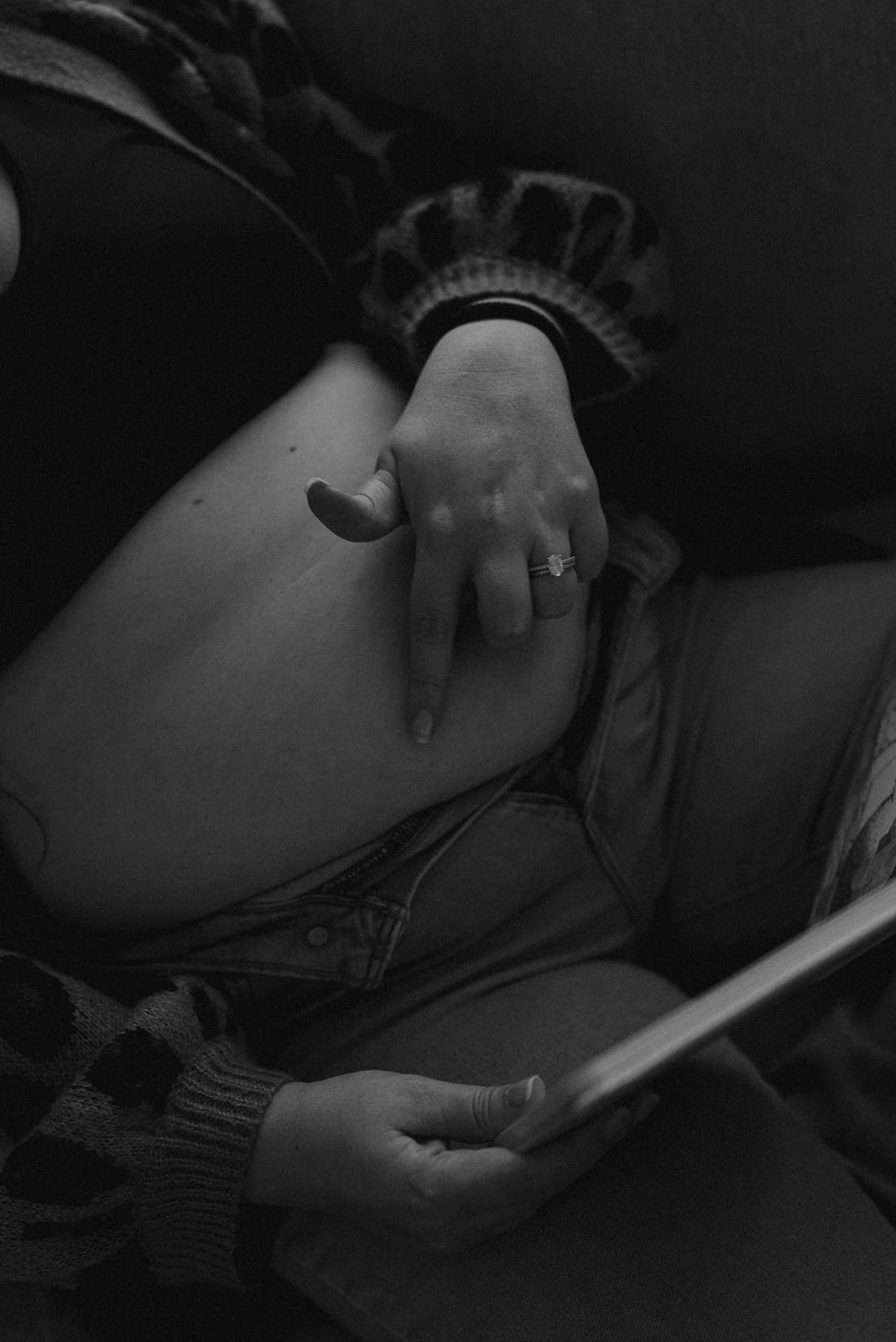 A person wearing a ring points to their bare belly while holding a book, shown in a black and white photo.