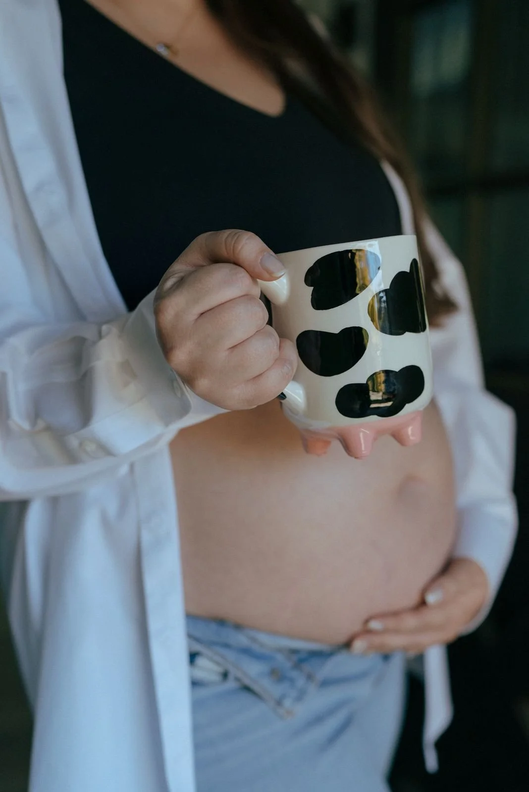 Pregnant woman standing barefoot in a doorway, wearing jeans, a black top, and an unbuttoned white shirt,  for a half baked pregnancy photoshoot