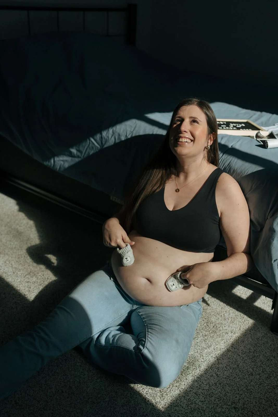 A pregnant woman sitting on the floor holding two baby shoes