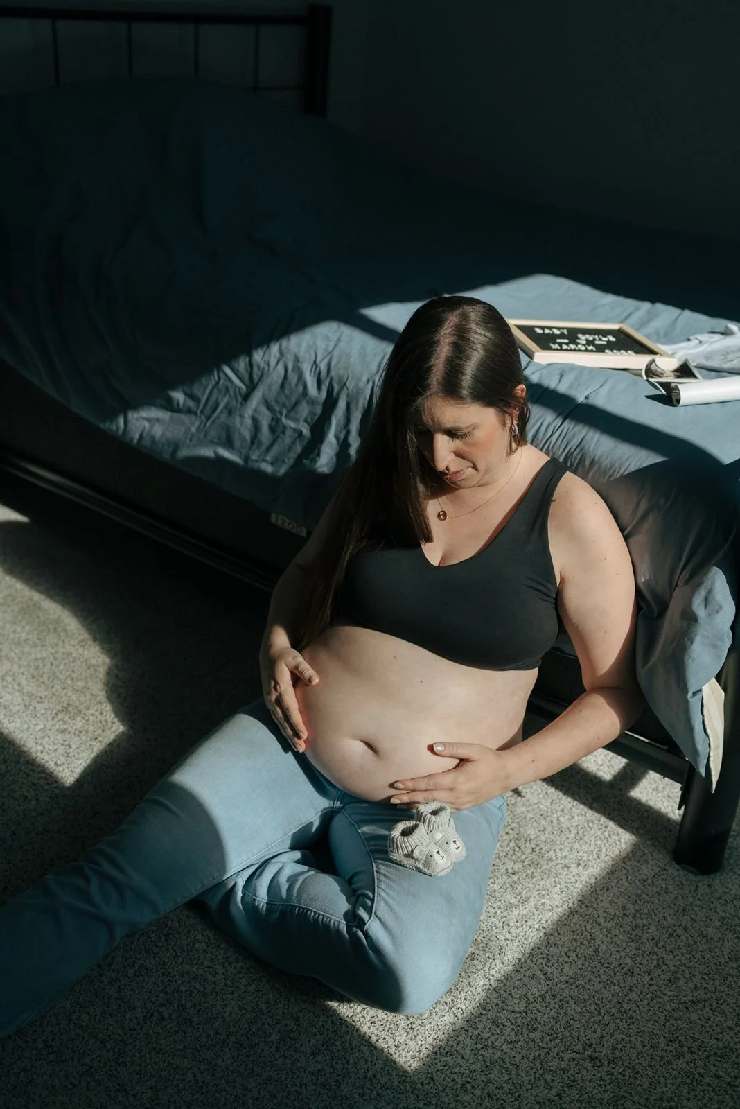 A pregnant woman sitting on the floor holding two baby shoes