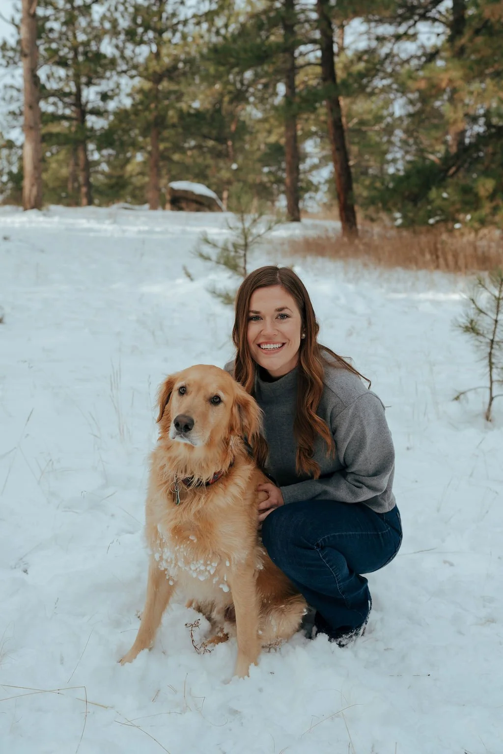 A man, woman, child, and a golden retriever stand together in a snowy forest with pine trees in the background for a documentary family photography session