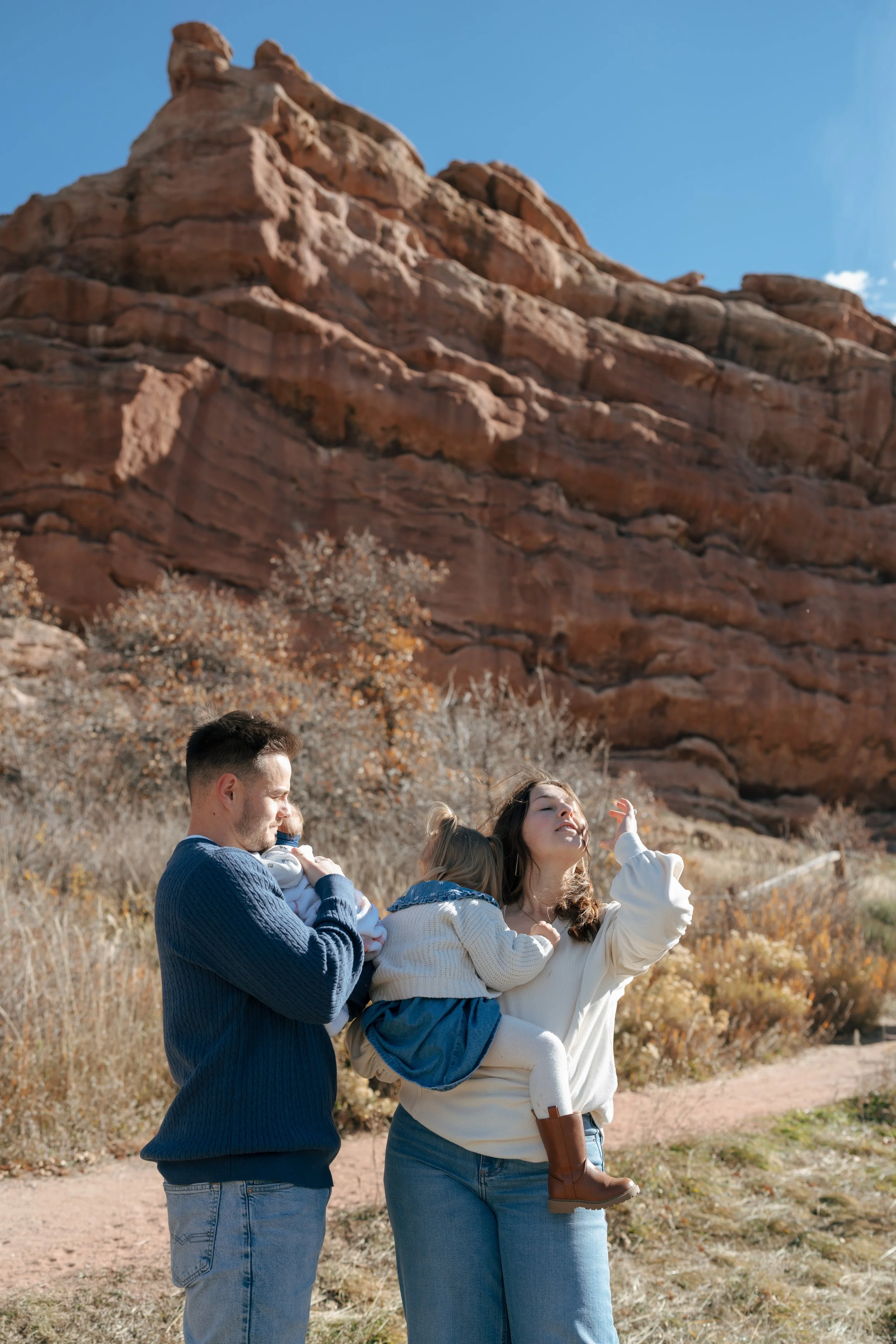 Denver Family Photographer takes a photo of a man and a woman with two small children in front of Red Rocks, Colorado