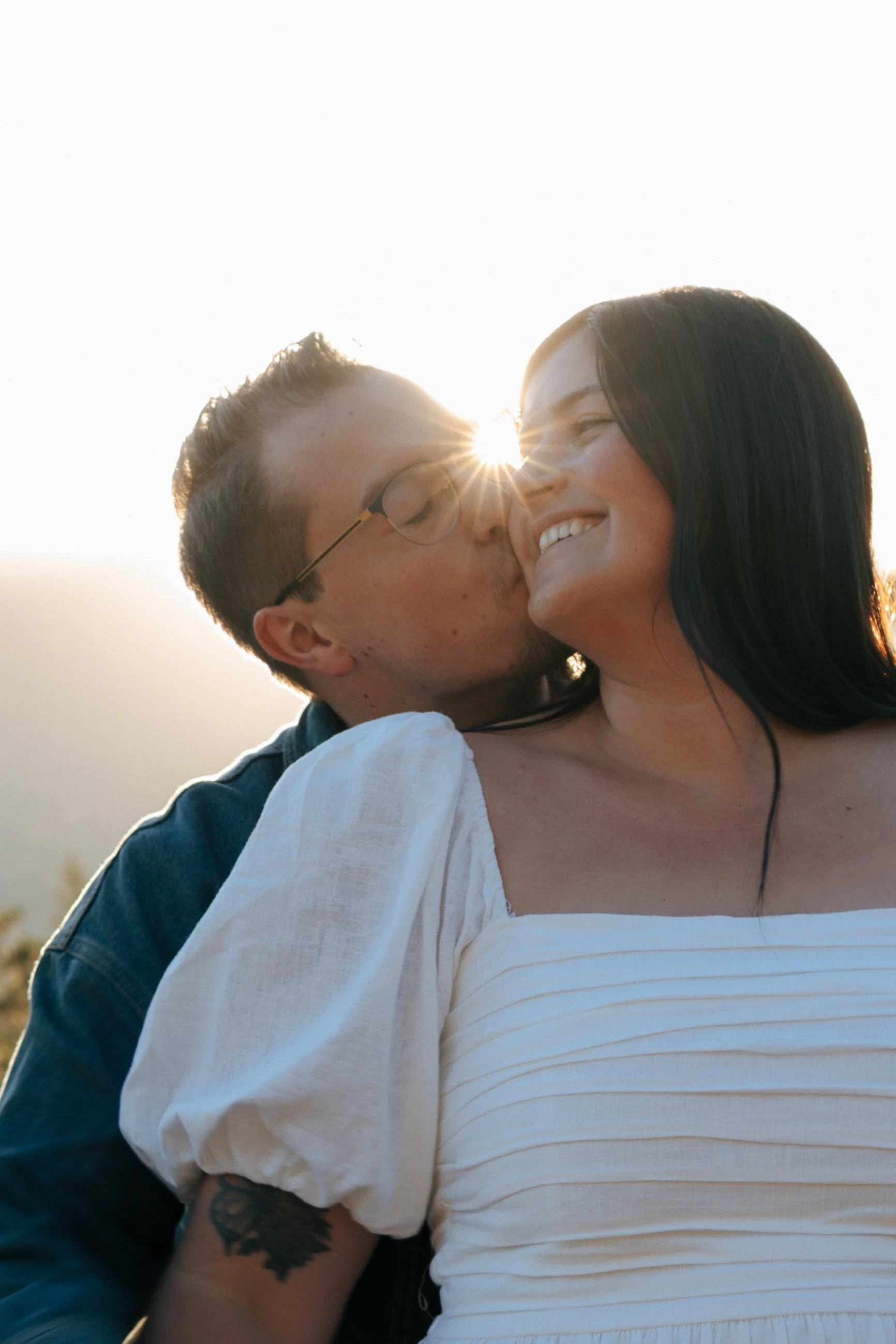 Man kissing woman's cheek with sun flare in the background.
