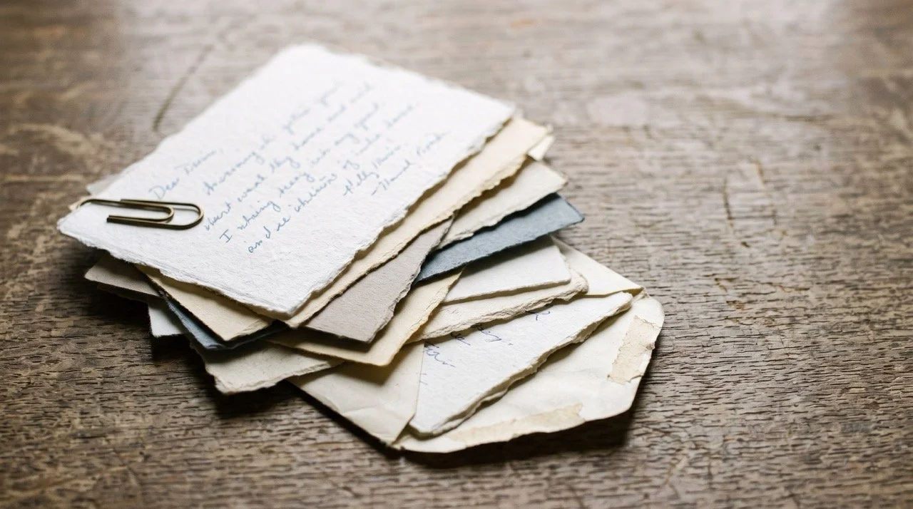 A stack of handwritten donor reply cards on a worn oak table in soft window light.