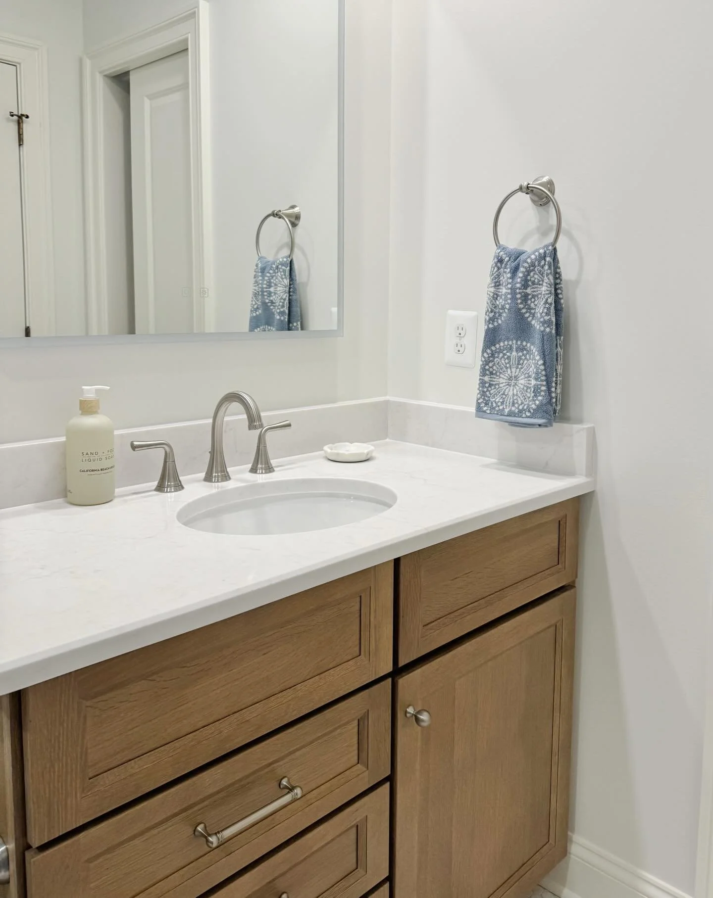 For this teen&rsquo;s bathroom we chose a beautiful oak vanity, lighted mirror, brushed nickel hardware, and pops of blue throughout. The result is fresh and modern with a hint of coastal.