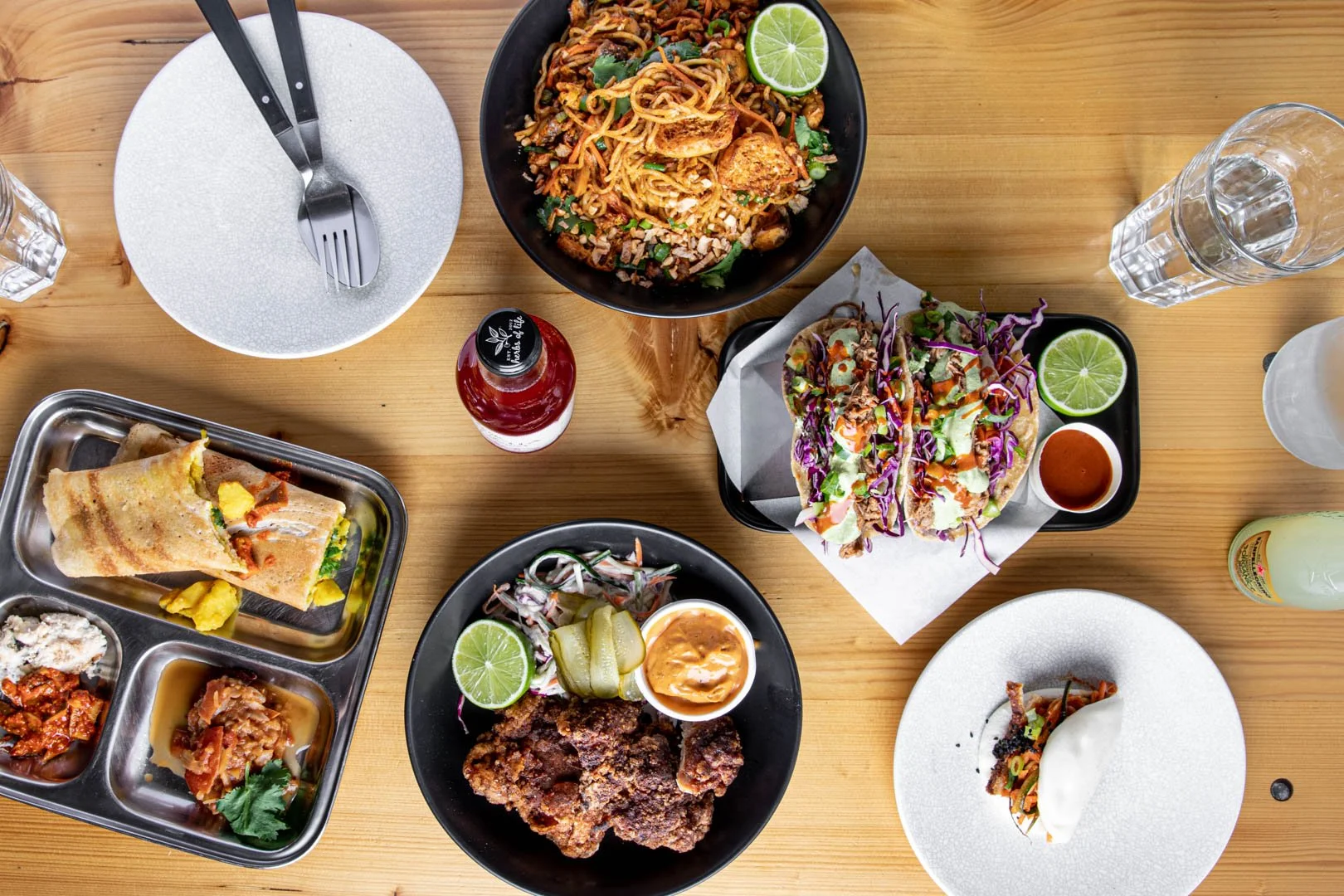 Assorted modern Asian dishes including tacos, noodles and fried chicken on a wooden table