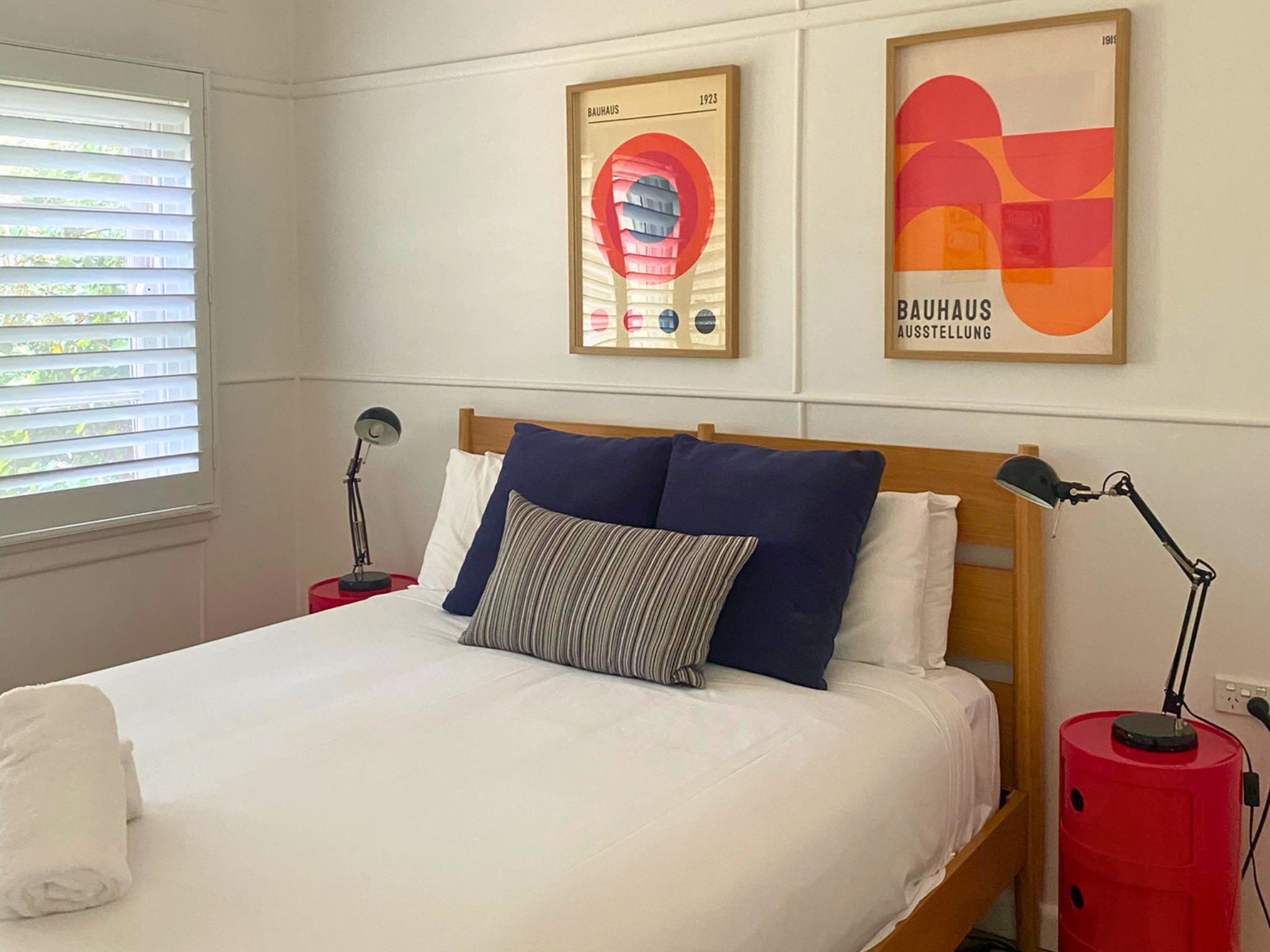 Stylish bedroom in Katoomba holiday cottage with wooden bed, crisp white linens, navy cushions and modern Bauhaus artwork.
