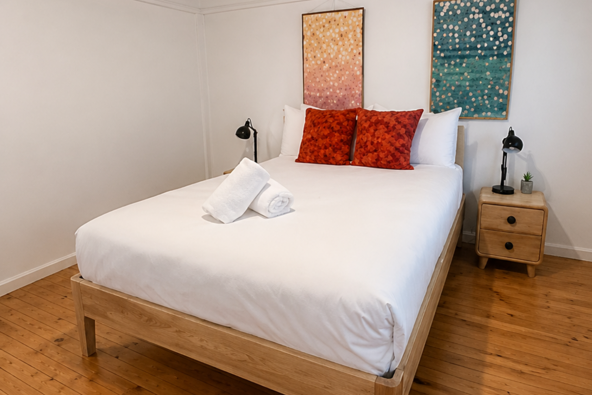 Comfortable bedroom at Katoomba holiday cottage with wooden bed, white linens, bedside tables and colourful wall art.