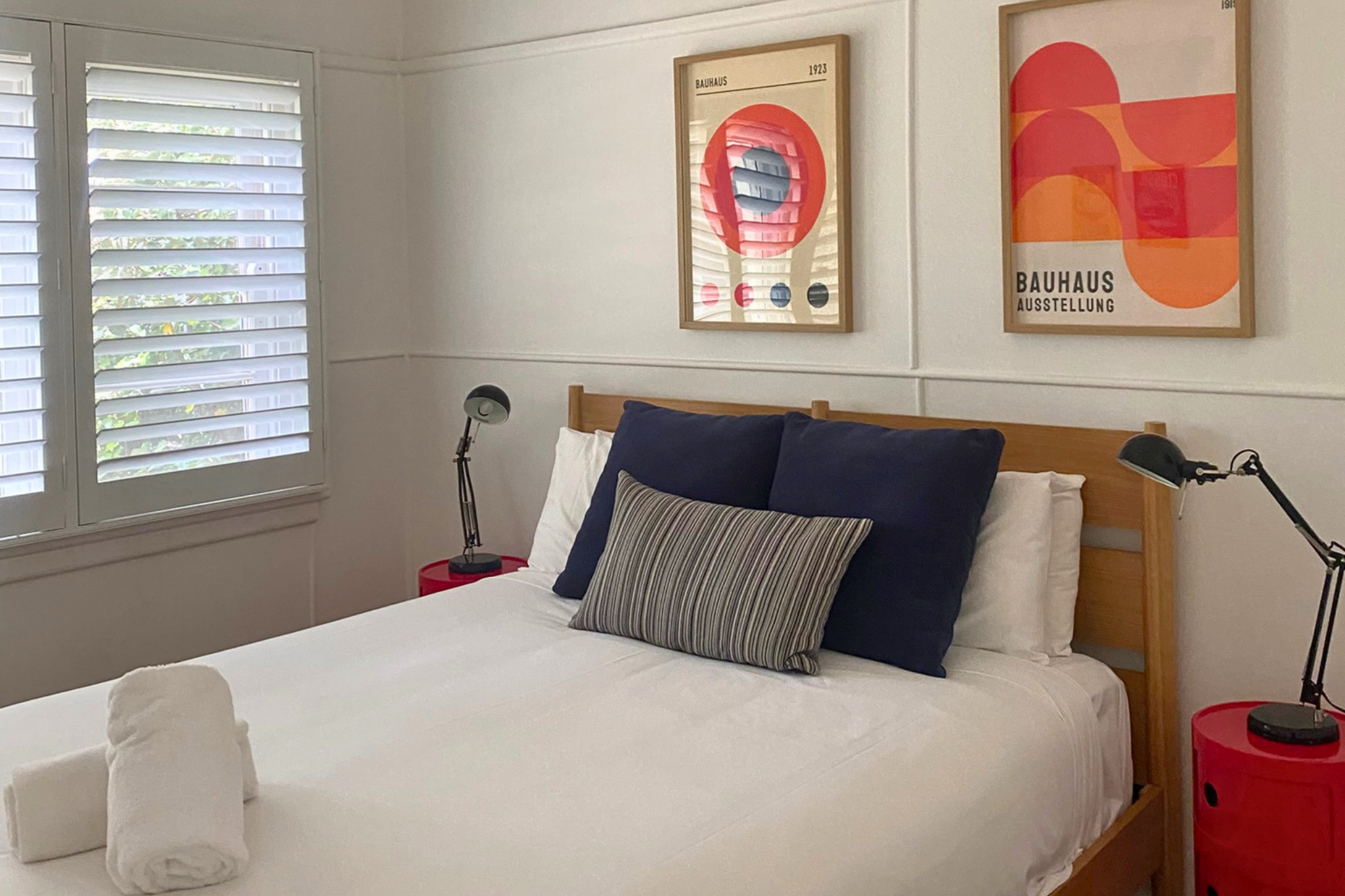 Comfortable queen bedroom at Katoomba holiday cottage with wooden bed, white linens, navy cushions and modern wall art.