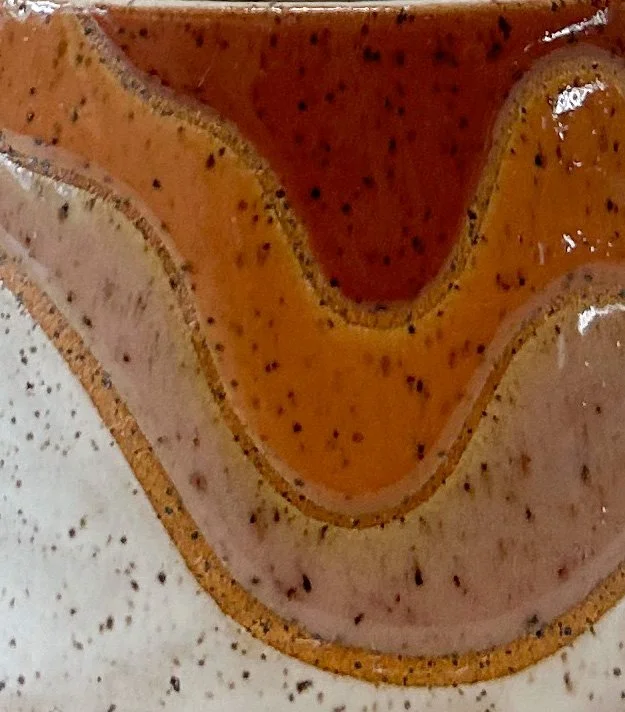 Close-up of a multi-layered, earth toned glazed mug on a speckled stoneware clay by Pye Ceramics.