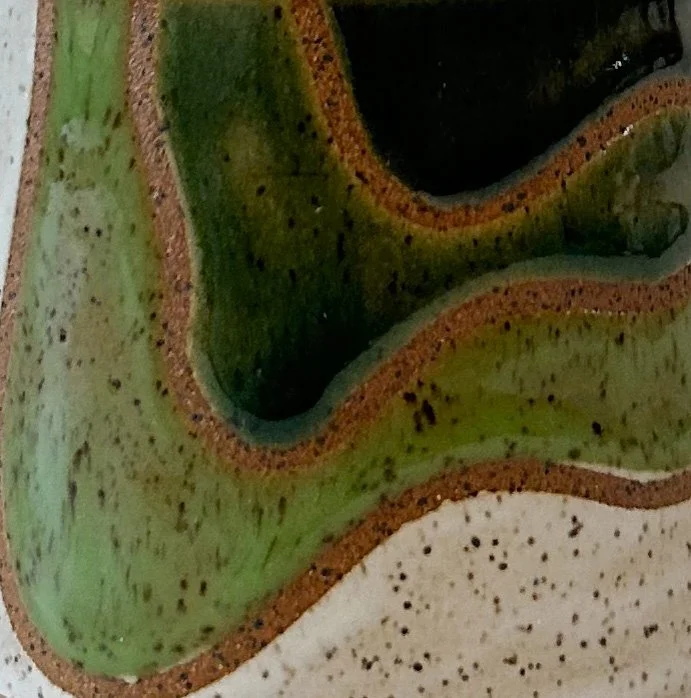 Close-up of a speckled stoneware mug with gradient green glazes and wavy topography lines.