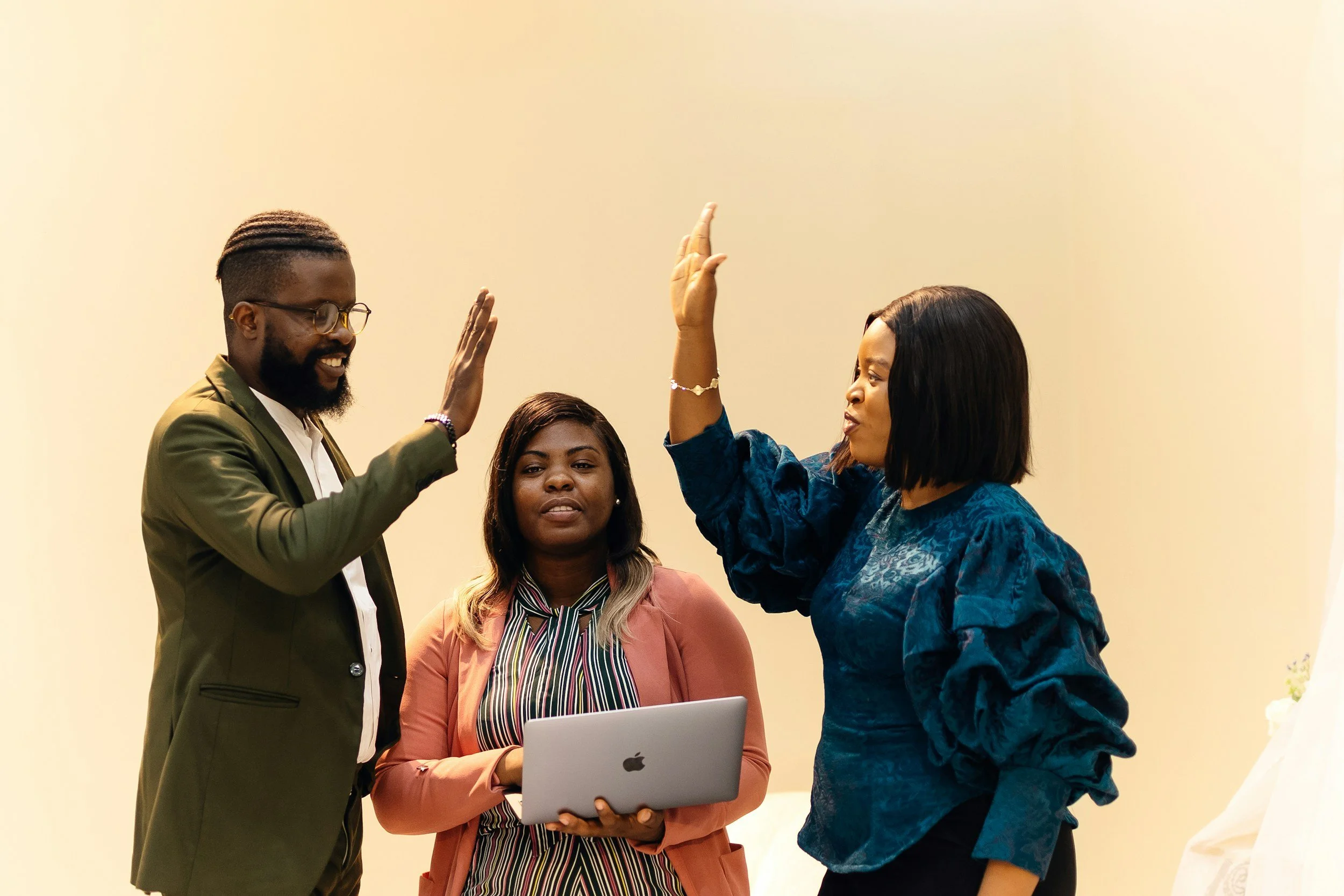 a group of people celebrating and about to give each other a high five with one person smiling in between them with a laptop computer