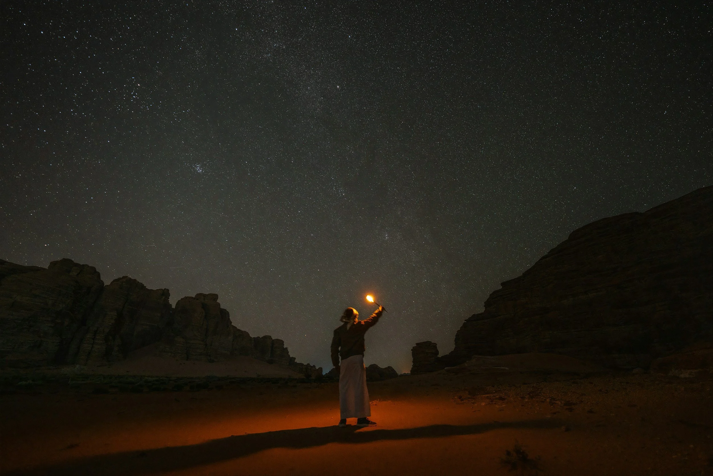a person standing in the expanse of the night sky with stars reaching out and up and holding a light above their head