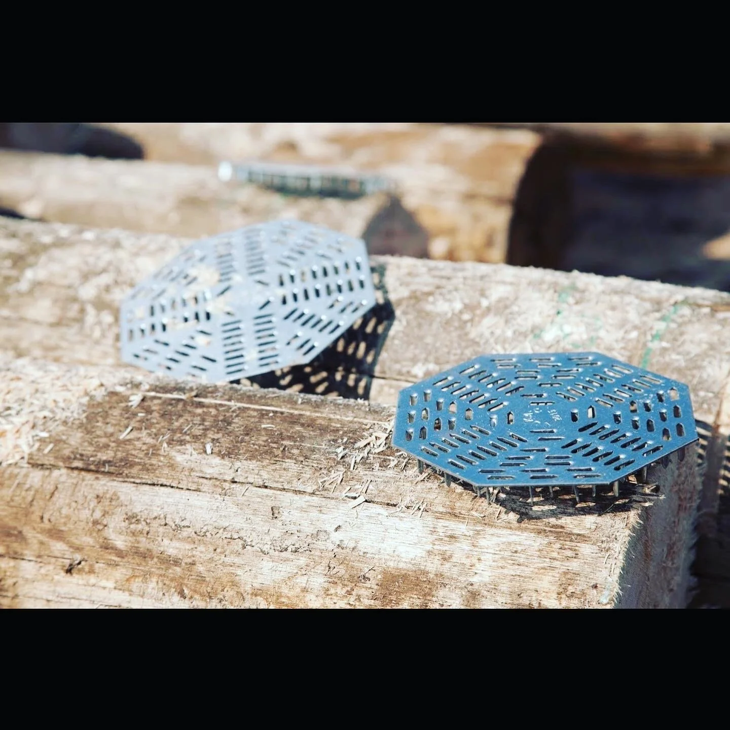 Two metal nail plates with perforated patterns on a wooden surface outdoors.