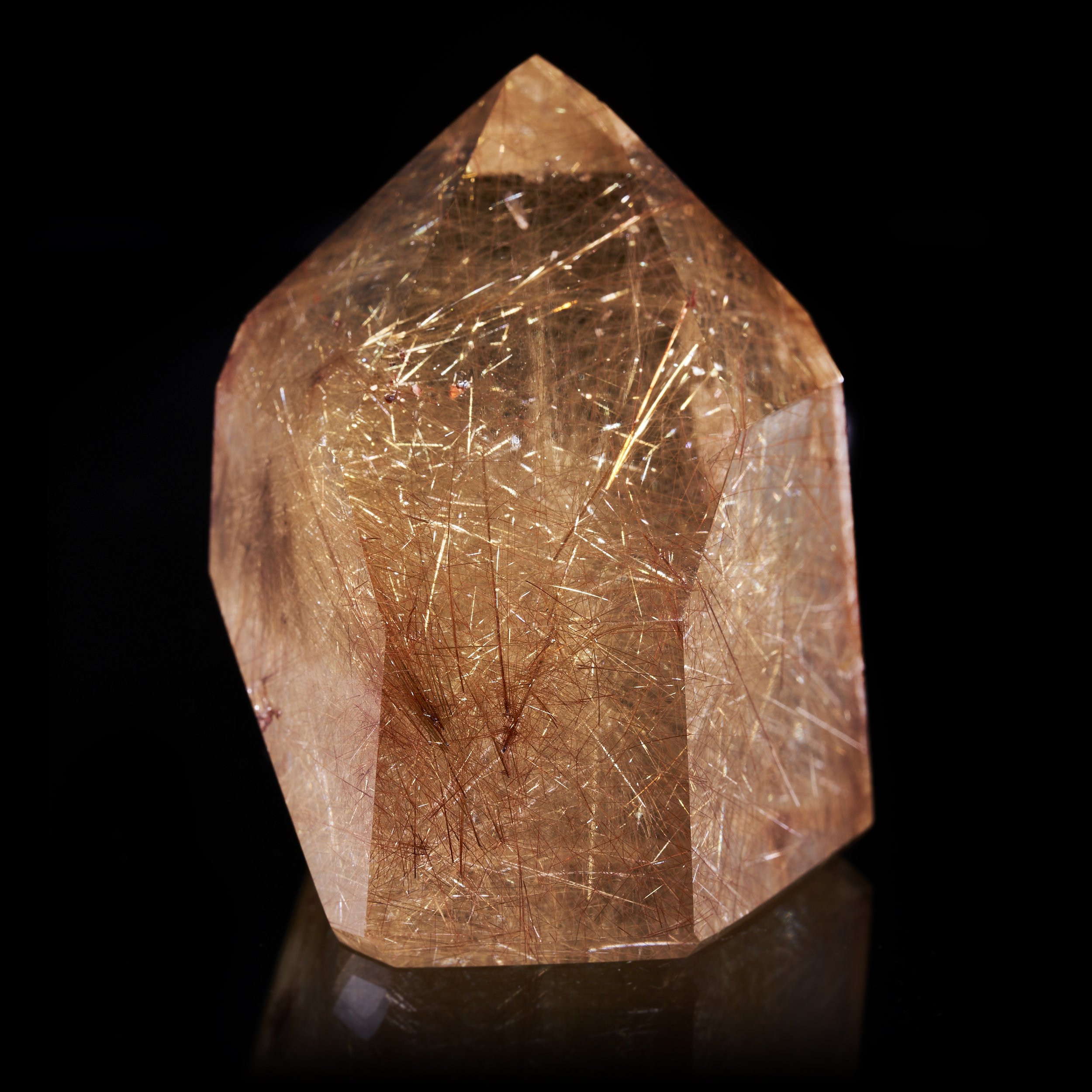 Image description: A front view photograph of a Polished Rutilated Quartz prism revealing golden and copper rutile needles within.