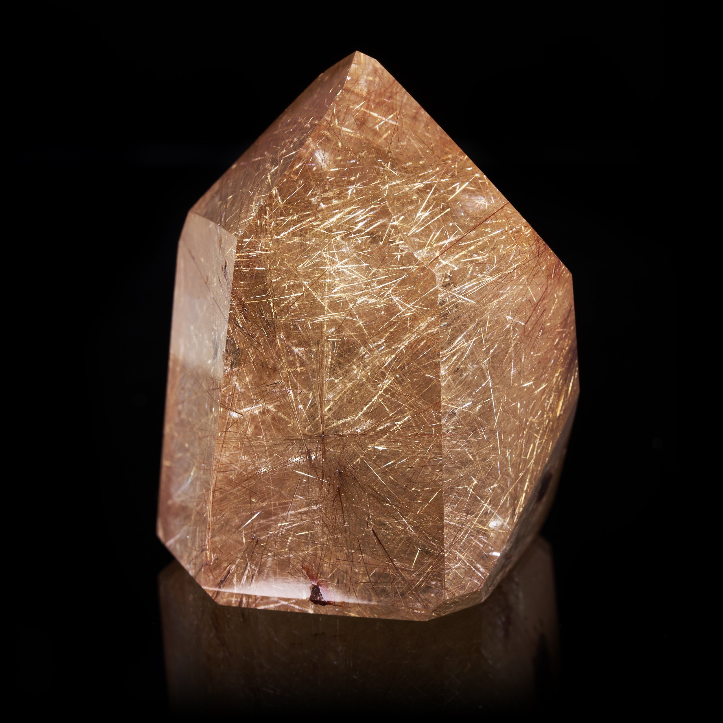 Image description: An alternative three-quarters view photograph of a Polished Rutilated Quartz prism revealing golden and copper rutile needles within.