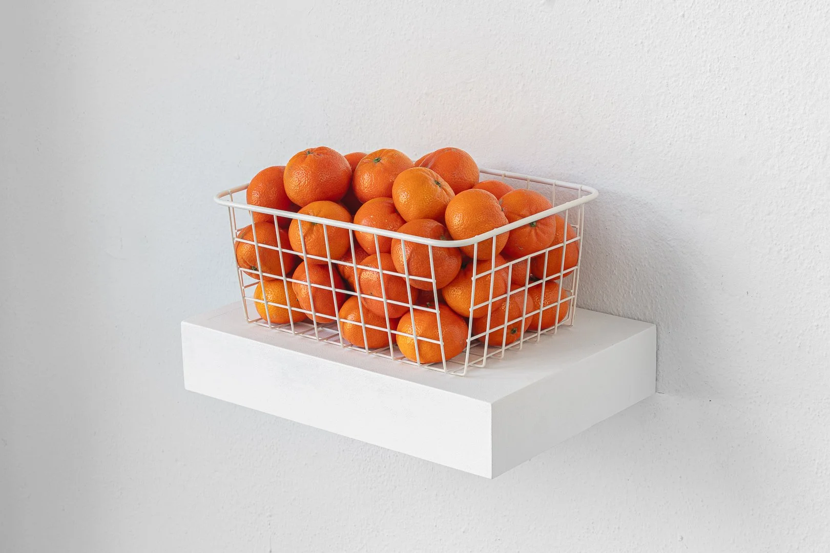 Silvia Koistinen, the smallness of things. Mandarins, wire basket, plate, shelves, glass with water and orange slice, miscellaneous glasses and cups, cloakroom tickets with text, bonbon wrapper, variable dimensions, 2026.