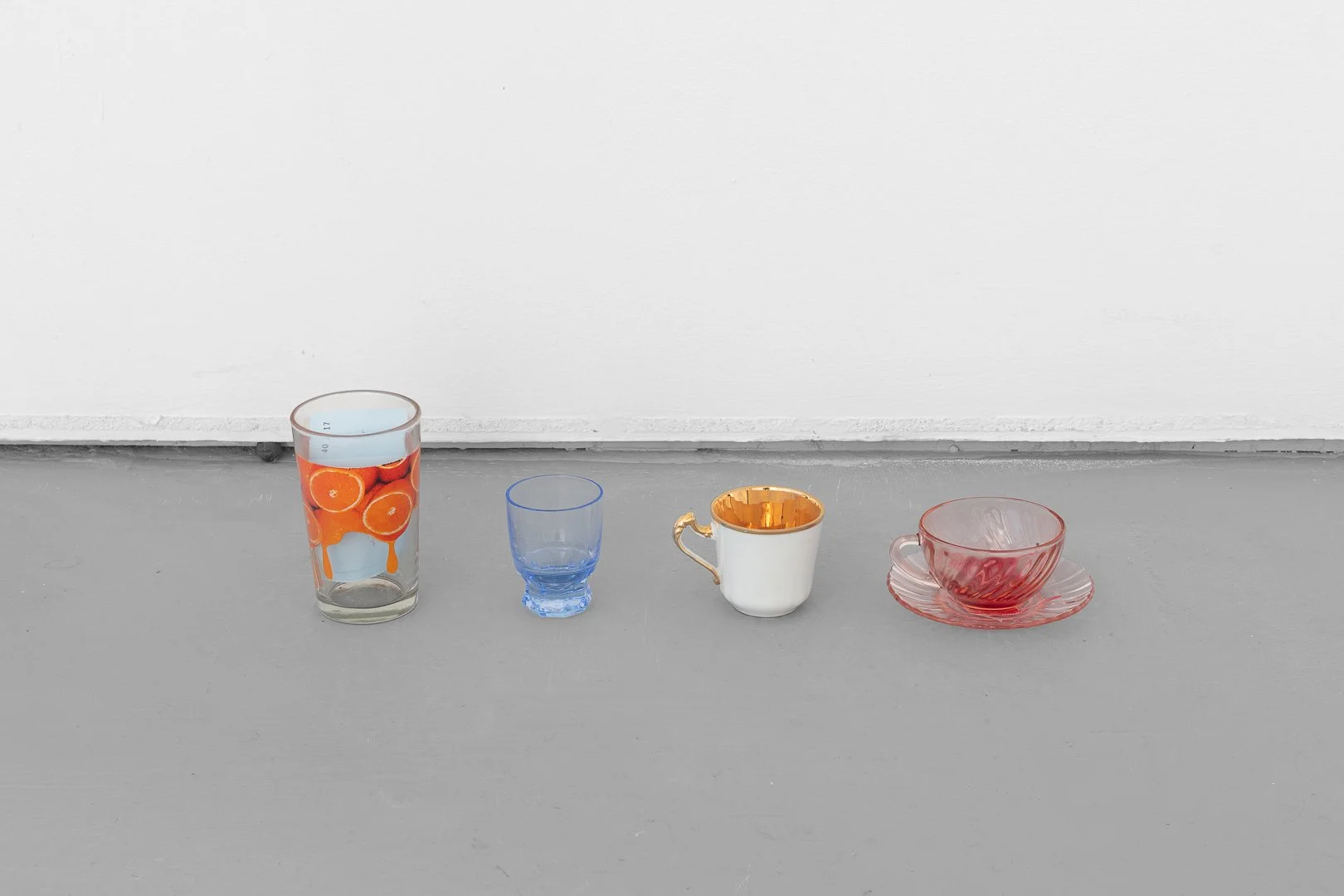 Silvia Koistinen, the smallness of things. Mandarins, wire basket, plate, shelves, glass with water and orange slice, miscellaneous glasses and cups, cloakroom tickets with text, bonbon wrapper, variable dimensions, 2026.
